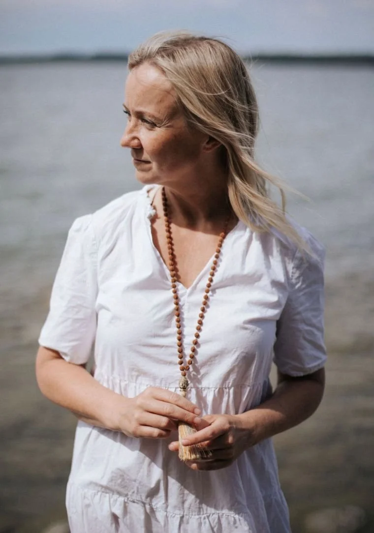 Nainen seisoo rannalla, taustalla vesi ja horisontti.