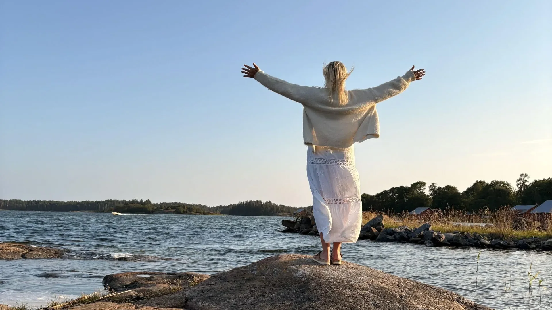 Nainen seisoo kalliolla, meren rannalla.