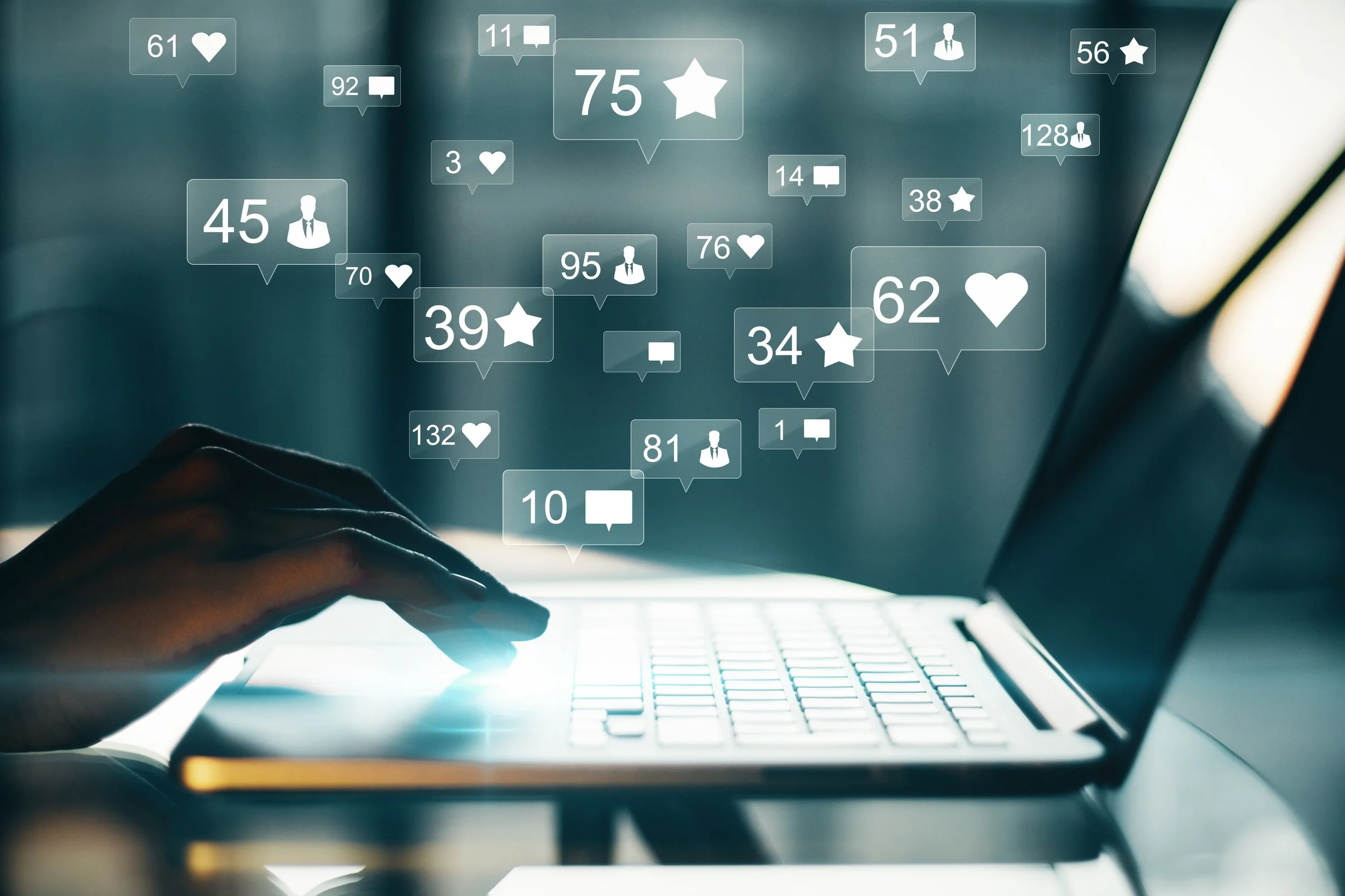 Close-up of a person's hand typing on a laptop keyboard with social media notifications and engagement icons floating above, including likes, comments, and followers.