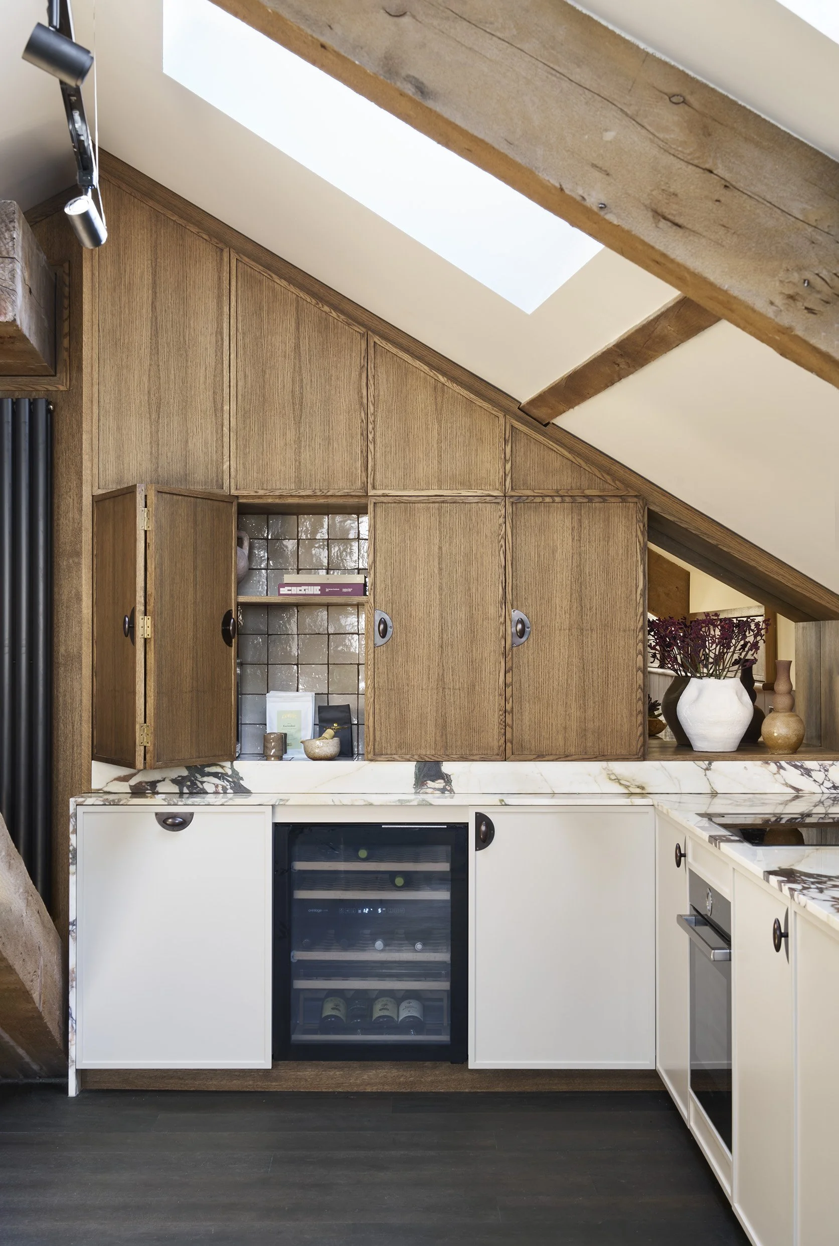 Kitchen with wooden cabinets, a wine cooler, and a marble countertop, under a sloped ceiling with skylight.