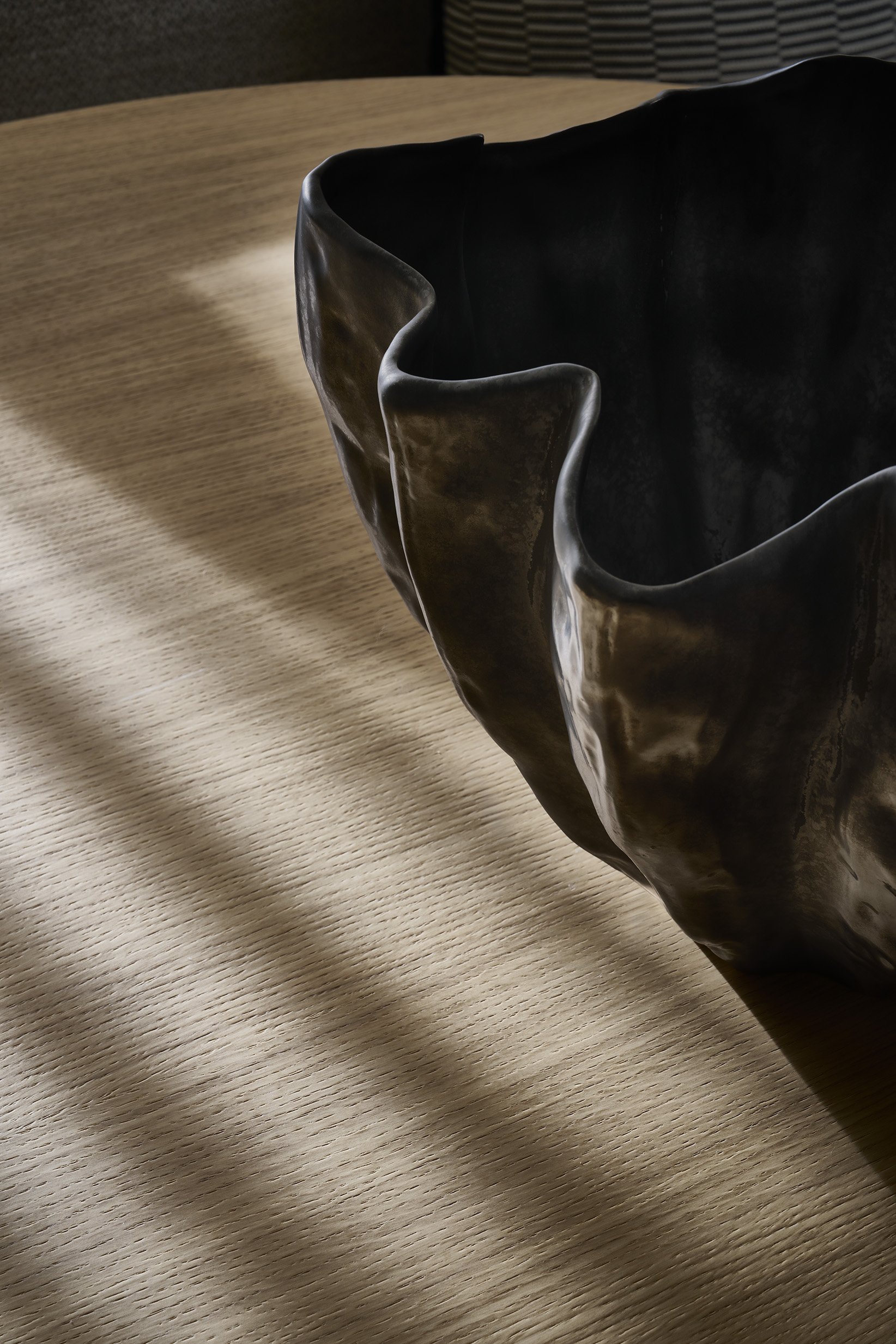 Close-up of a black, wavy-shaped ceramic or metal sculpture on a wooden surface, with shadows cast across the table.
