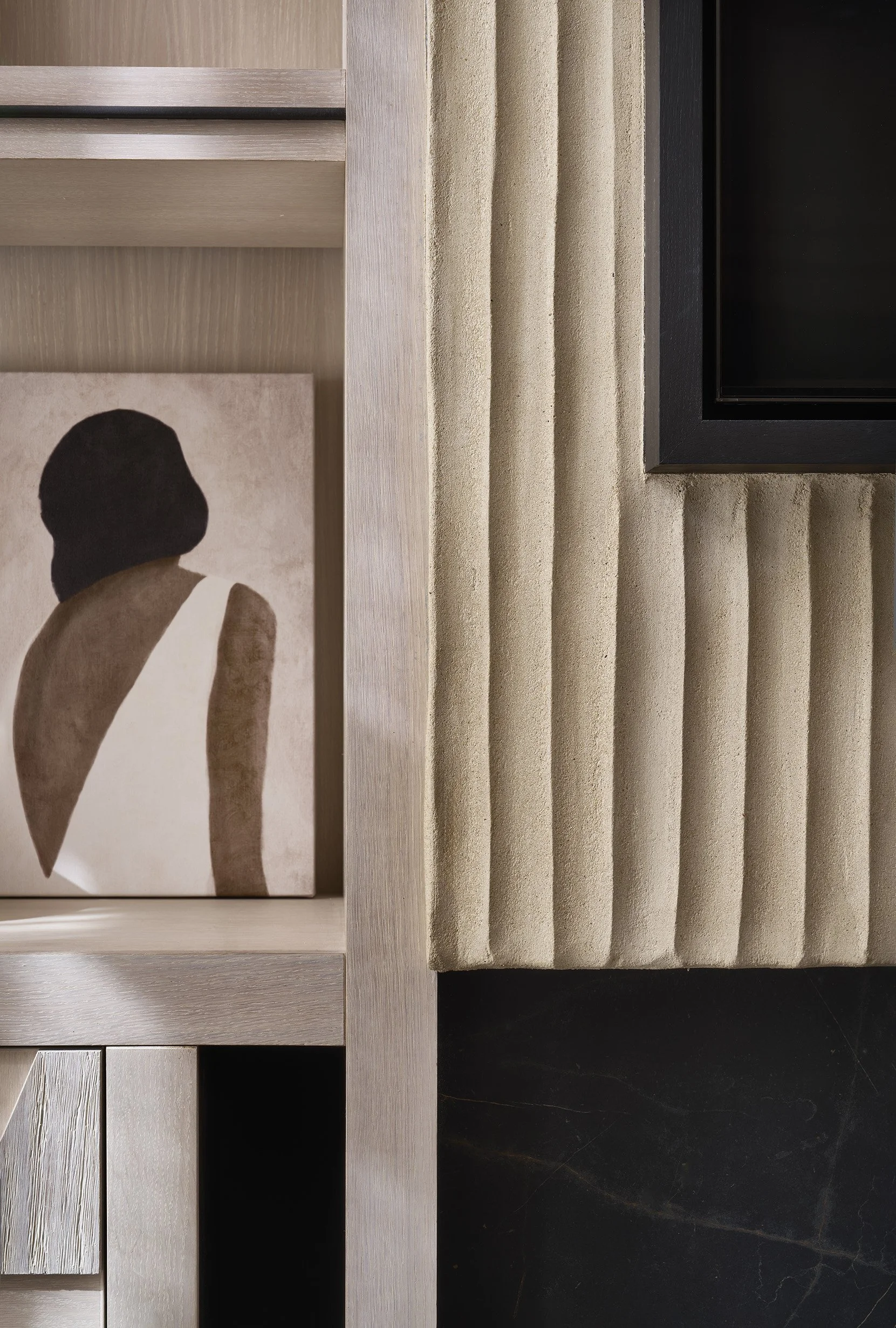 Close-up of a modern interior shelf with a framed art piece showing the silhouette of a woman and a section of textured, ribbed wall paneling next to a black-framed display or television.