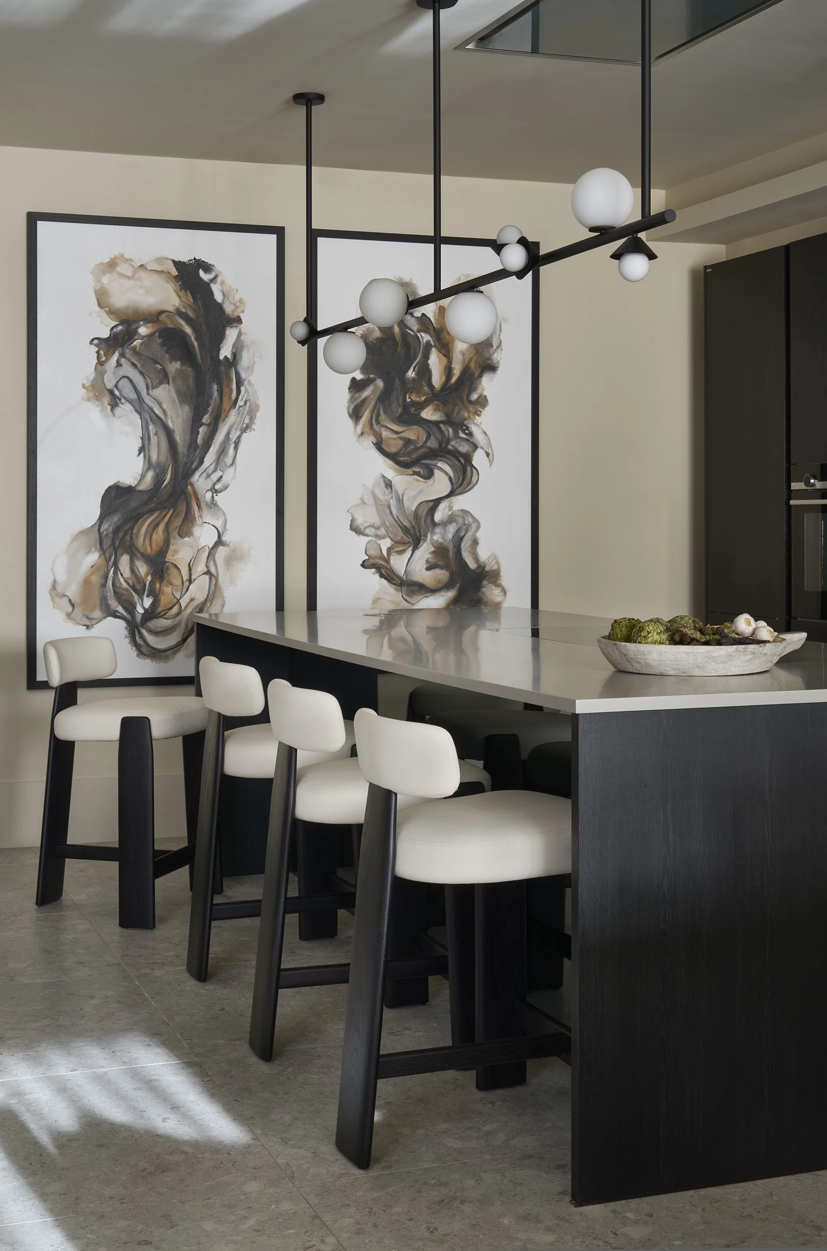 Modern kitchen with black and white chairs around a kitchen island, abstract artwork on the wall, and a contemporary chandelier.