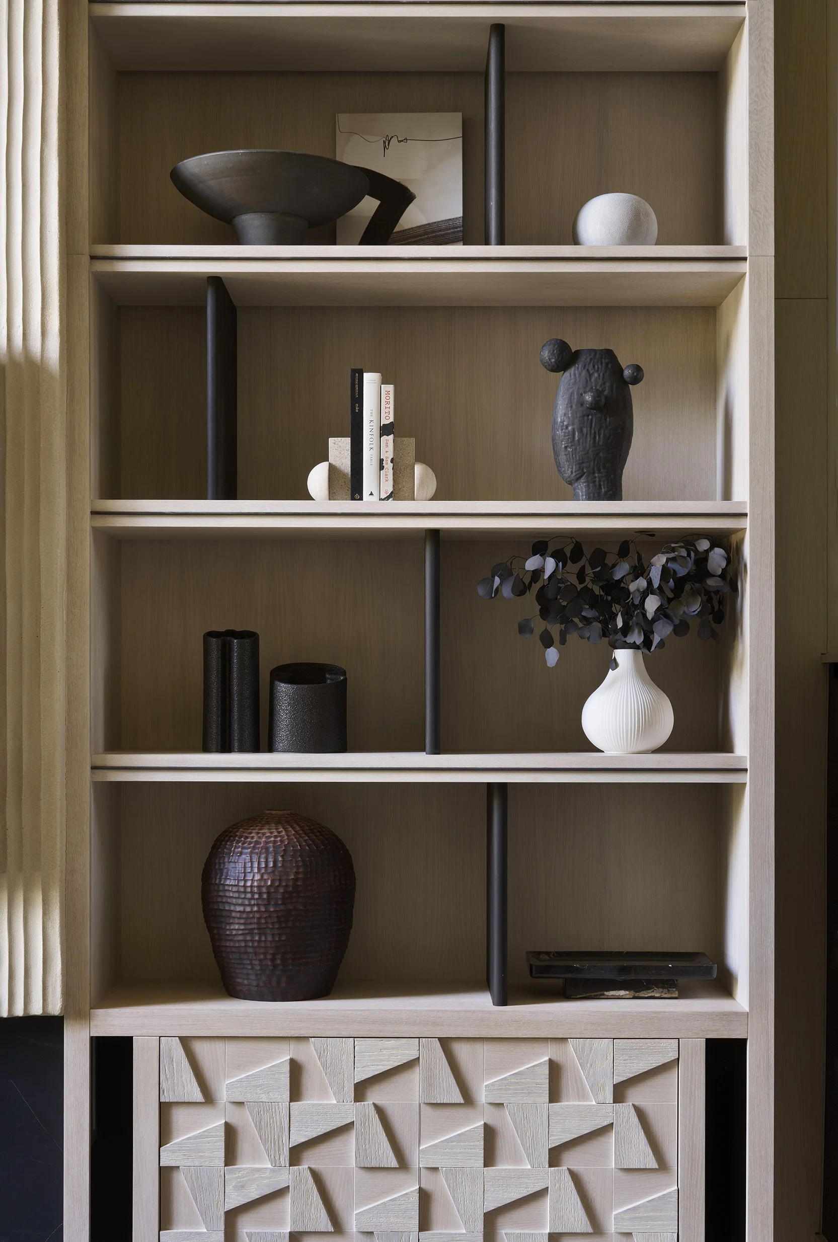 A wooden bookshelf filled with various black and white decorative objects, books, vases, and sculptures.