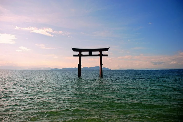 Portale torii tradizionale giapponese parzialmente sommerso dall'acqua nel mare con un cielo sereno e alcune isole sullo sfondo.