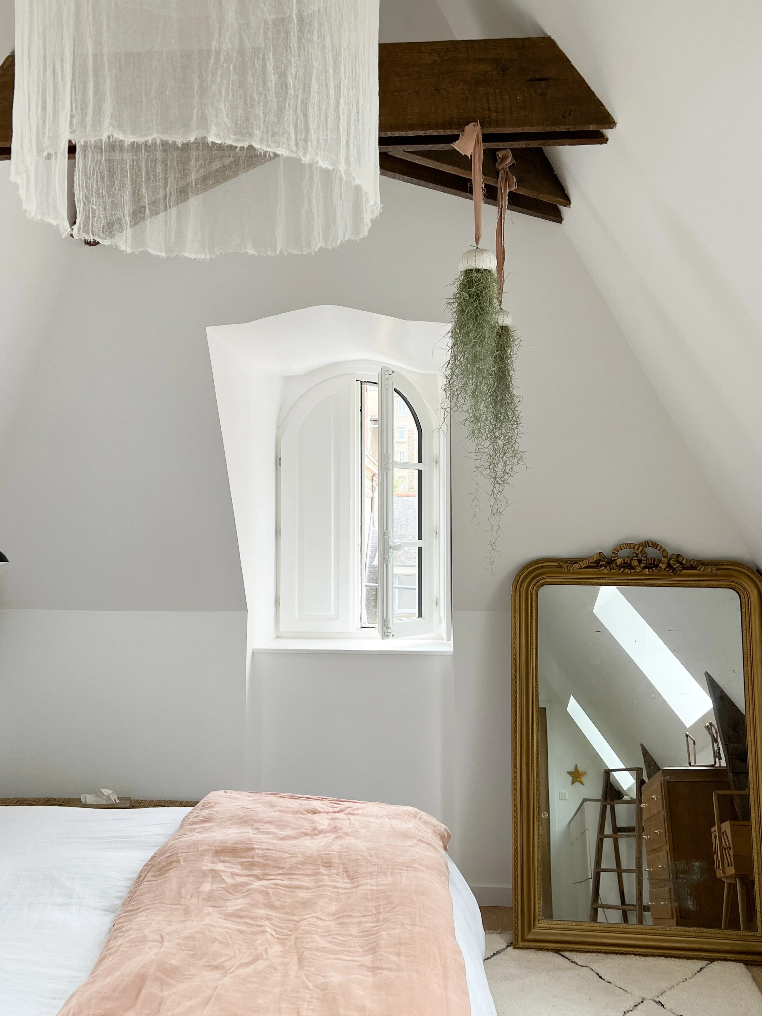 Chambre avec lit, grande cheminée, miroir ancien, fenêtre arquée et décoration en bois.
