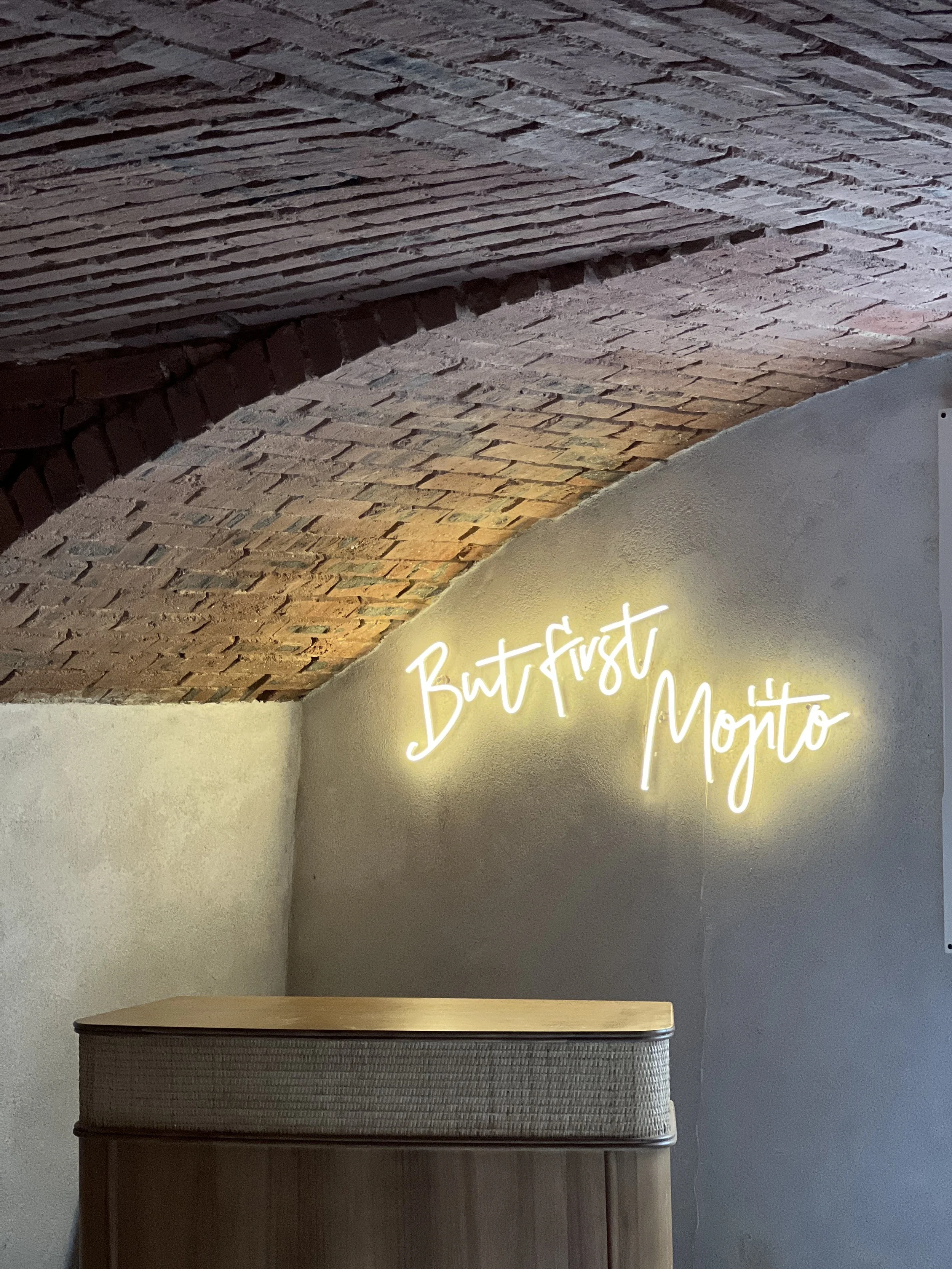 Mur en briques avec un plafond en briques apparentes, éclairé par un néon écrit 'BudFrost Monto'.