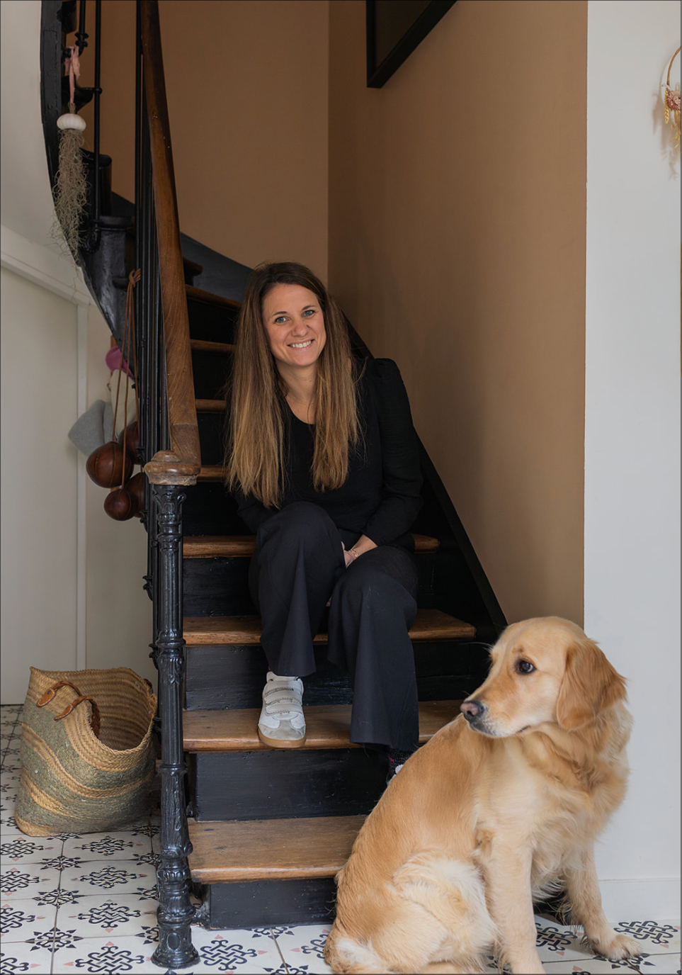 Une femme assise sur un escalier en bois avec un chien golden retriever à ses pieds, dans une maison