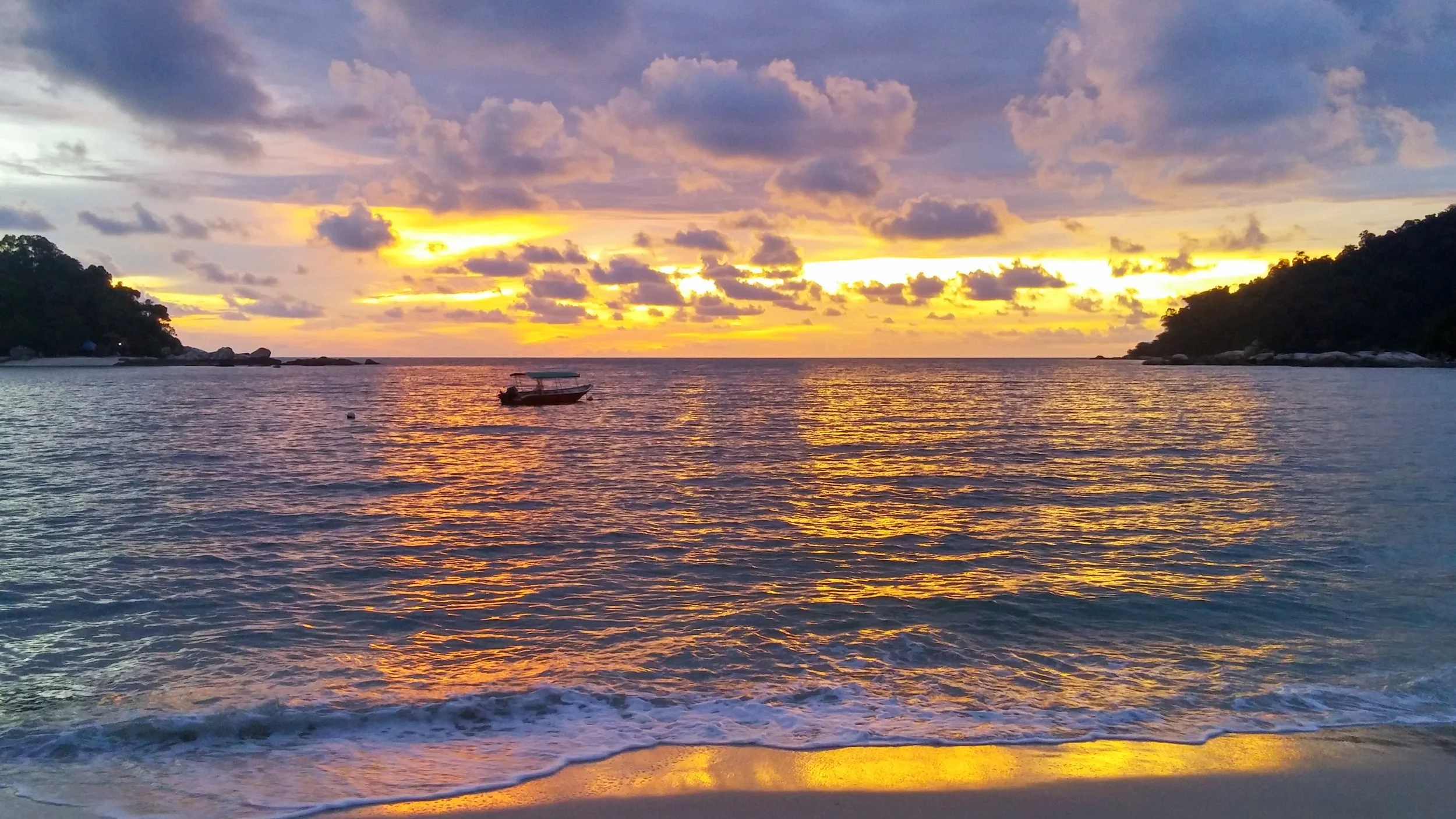 A single fishing boat in the water while a vibrant sunset is lighting up the sky and sea
