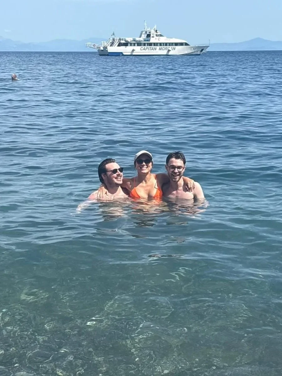 Megan, Tyson and Patrick swimming in the clear waters on the amalfi coast. Megan wears grey ball cap sunglasses and orange bikini, the boys both wear glasses