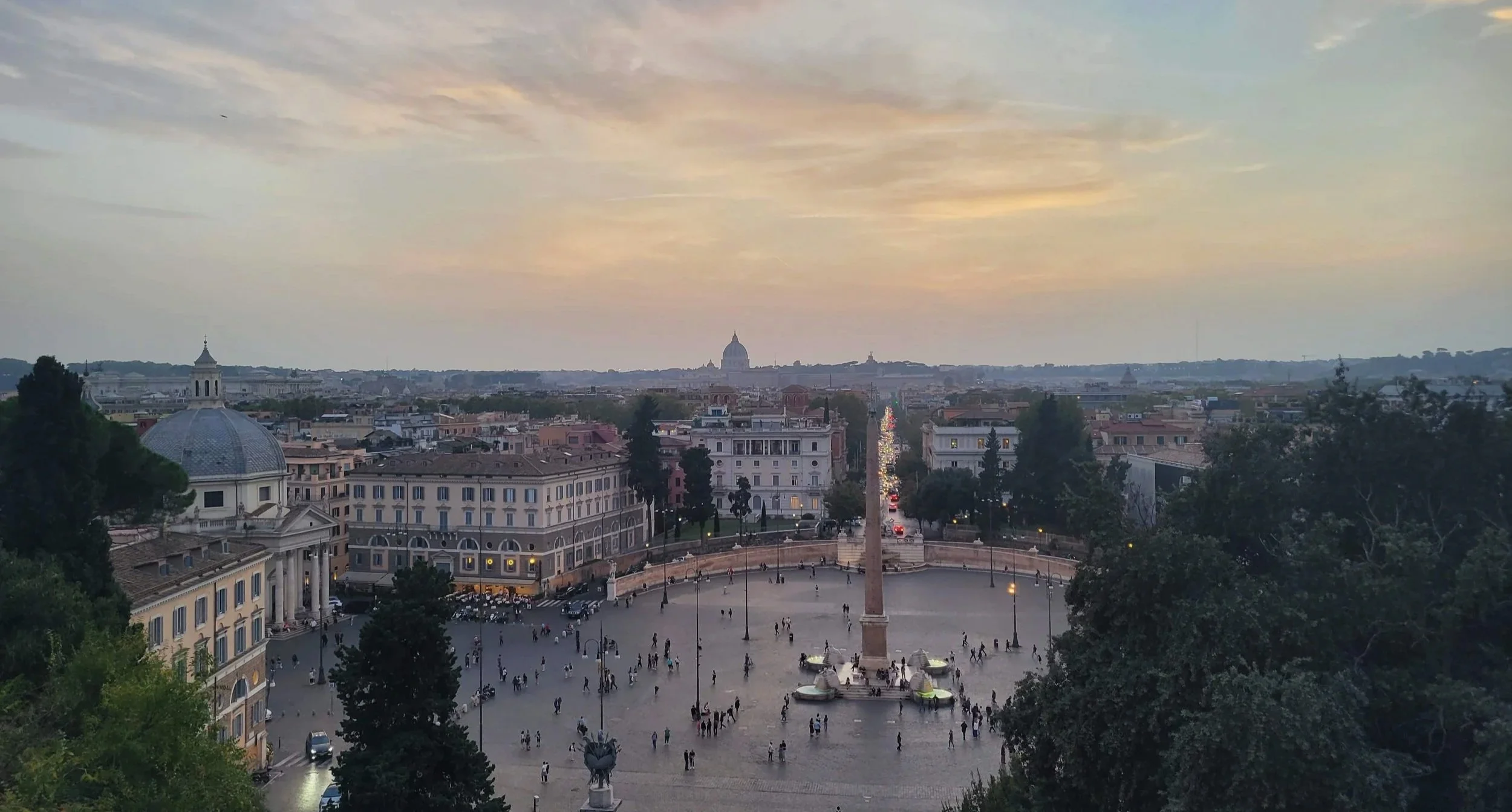 A soft pastel coloured sky at sunset giving a gentle glow to the square and city below. St Peter's Basilica is visible in the background.