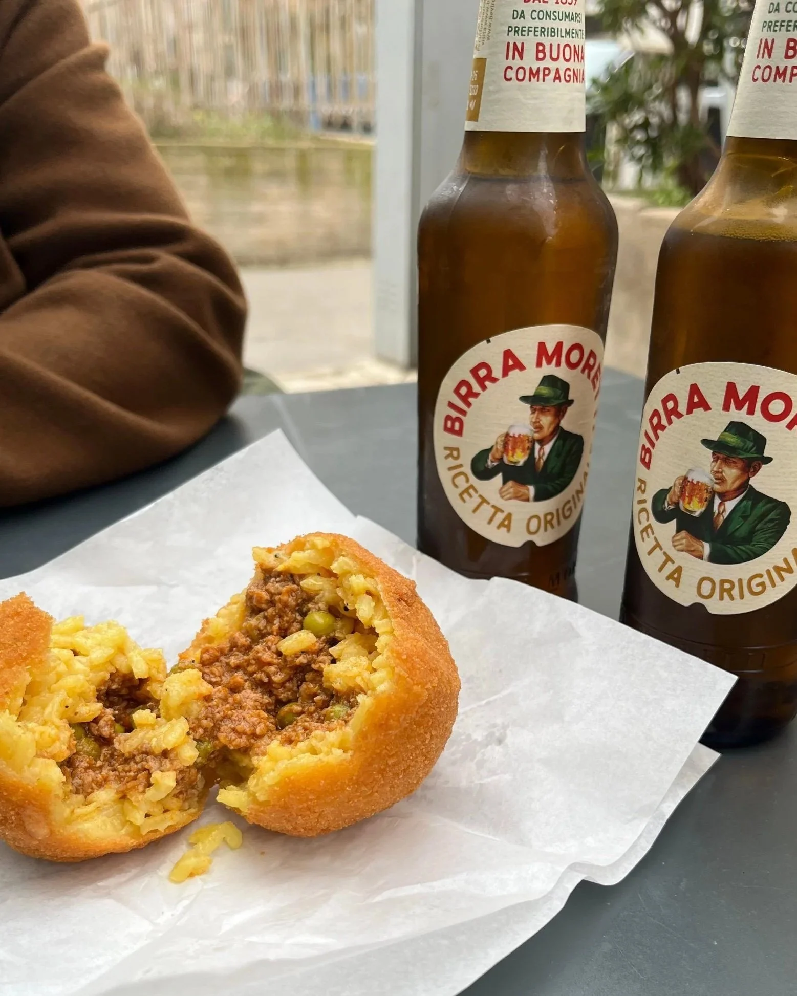 an arancina on white takeaway bag and two birra Moretti bottles