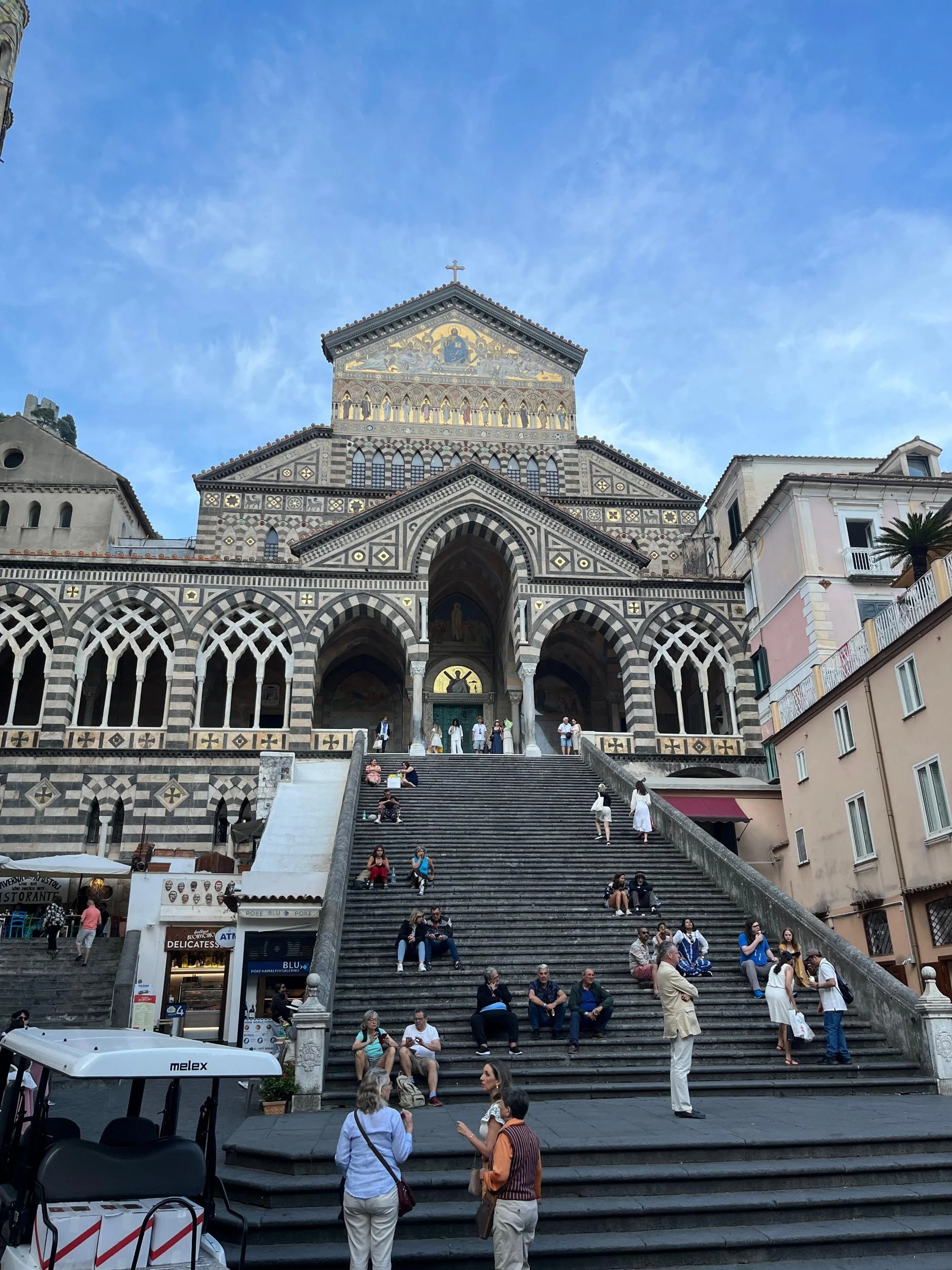 people sitting on the steps of the amalfi duomo, taking in the activity in the square