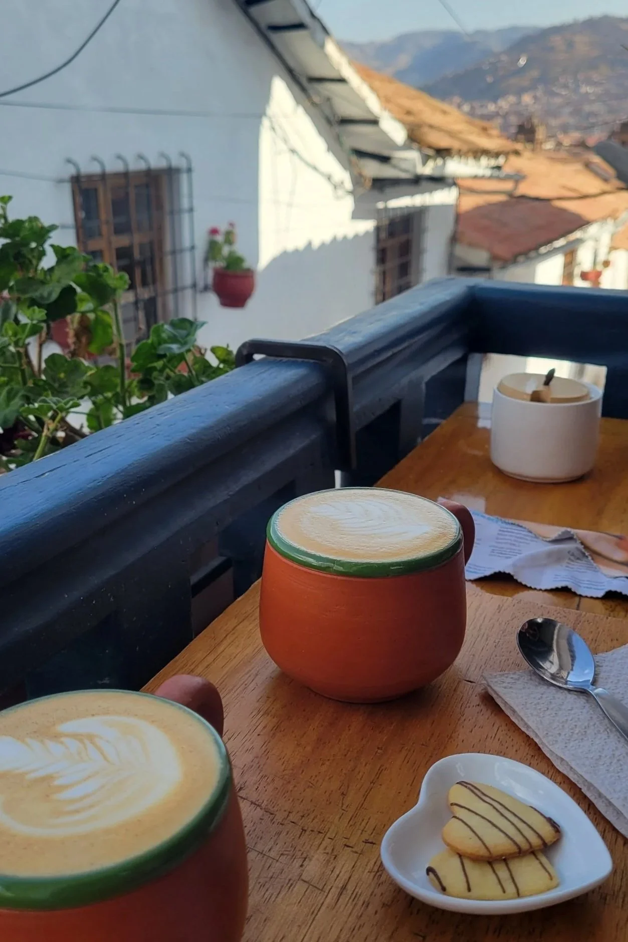 two cappucinos on a balcony bar with the view of cusco and mountains in the distance