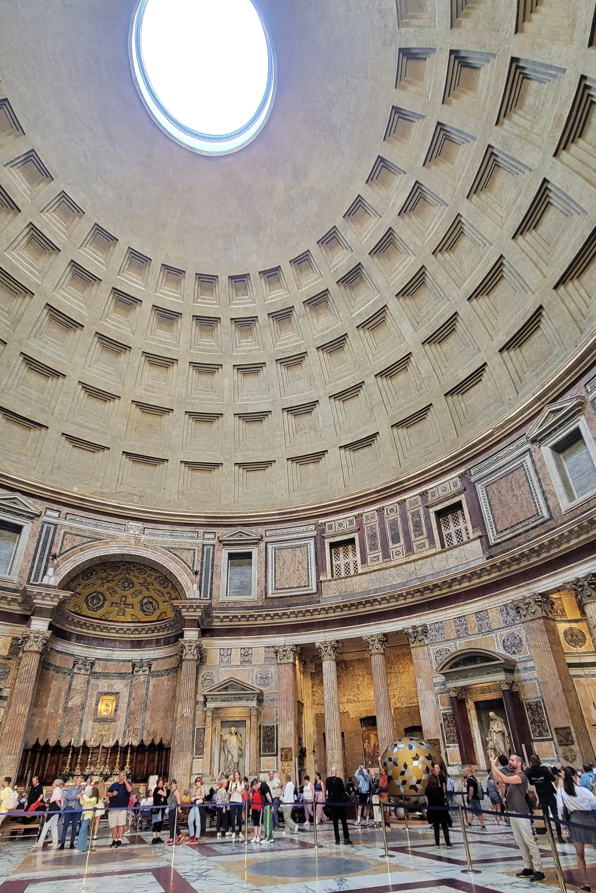 An interior shot of the Pantheon in Rome, Italy. The dome sctructure shows hollowed out squares and a large circular hole in the top.