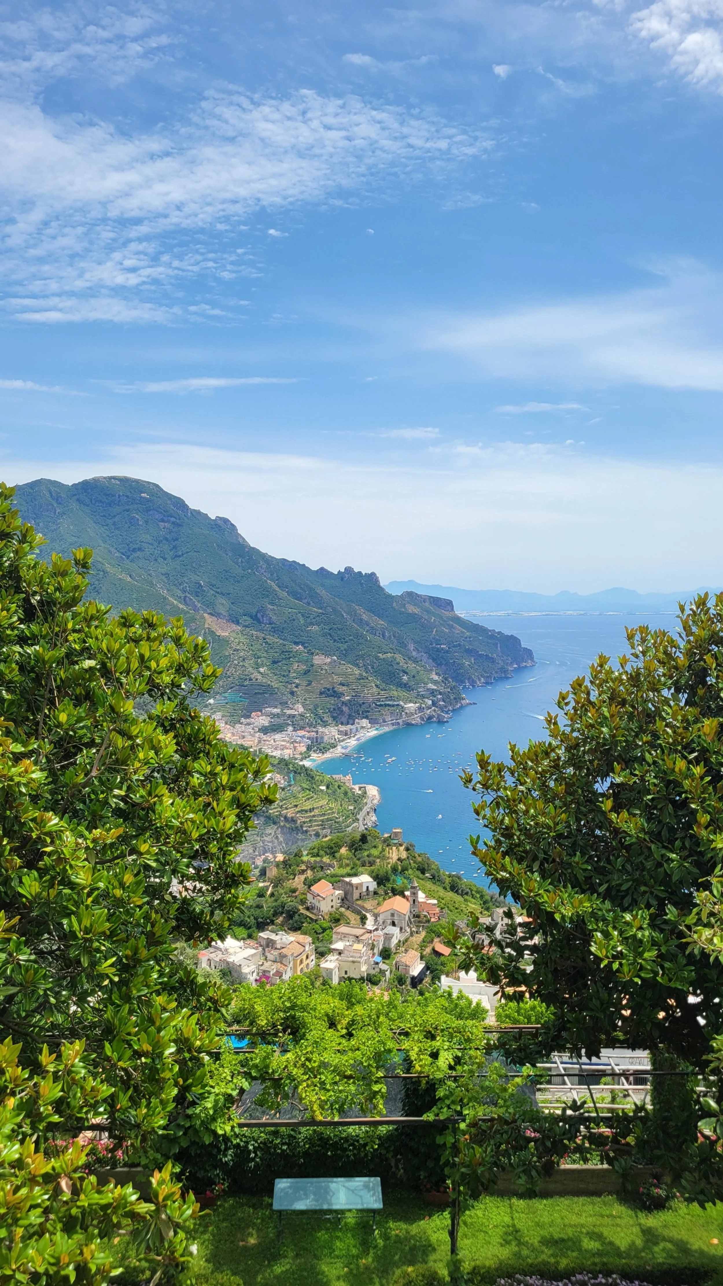 Blue ocean dotted with white boats below. terraced hills of lemon trees run along coast. can see towns nestled into hills