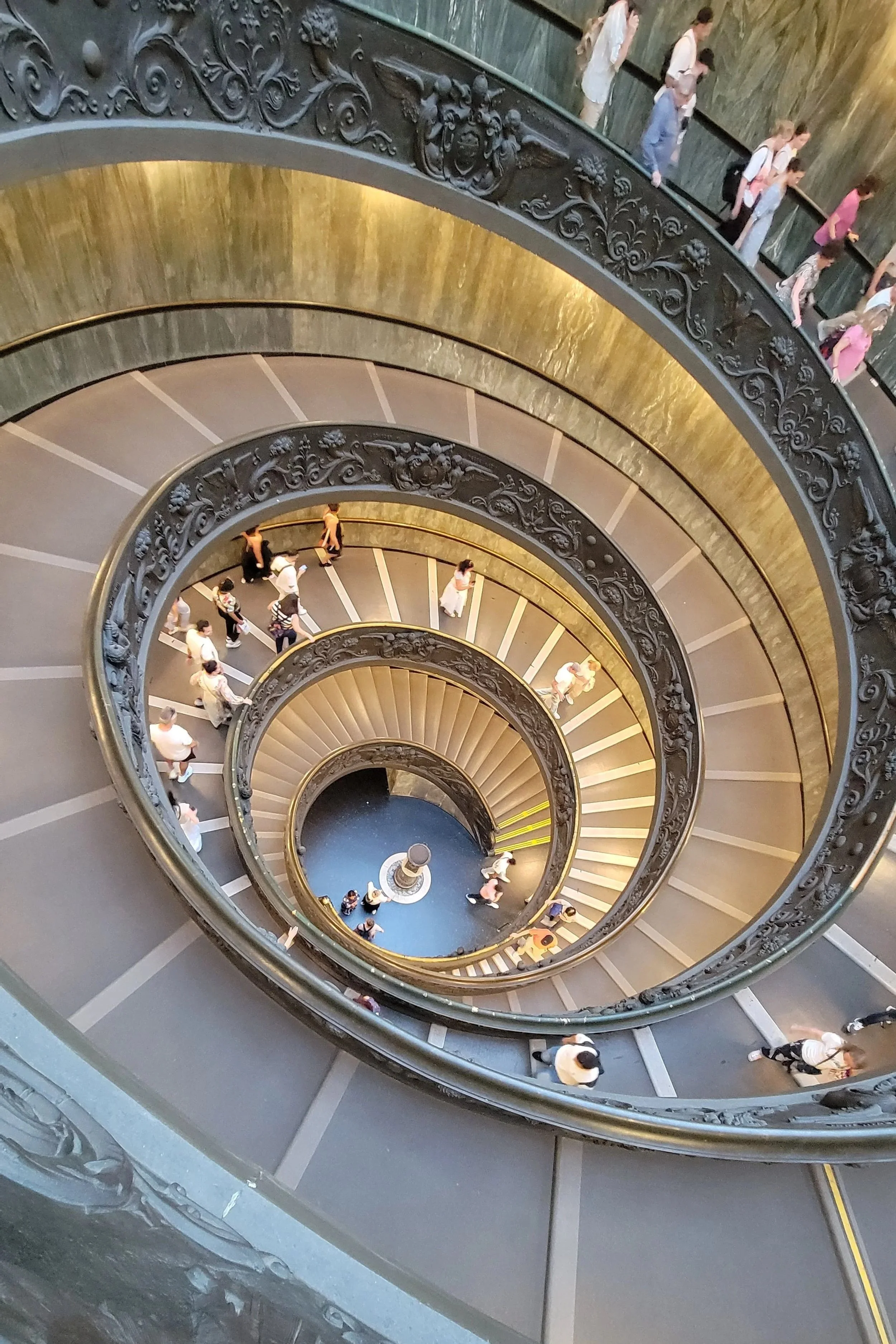People walking down the Bramate Stairs in the Vatican Museums. The ovular spiral stairs create a unique view looking down through the tightening spirals.