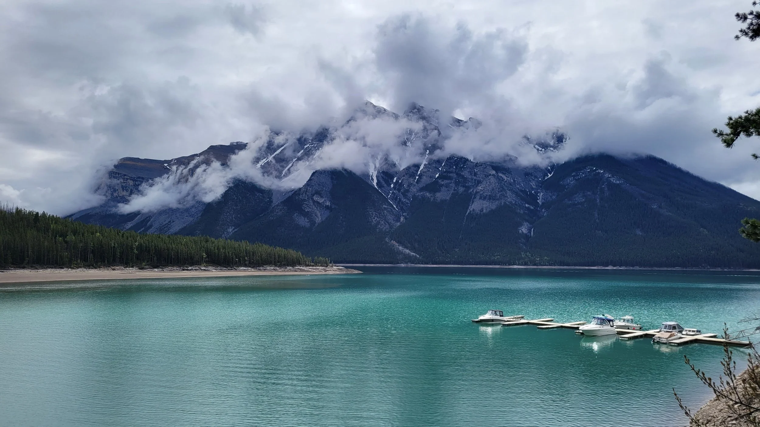 a green-blue glacier-fed lake with low hanging clouds covering the mountains in the distance.