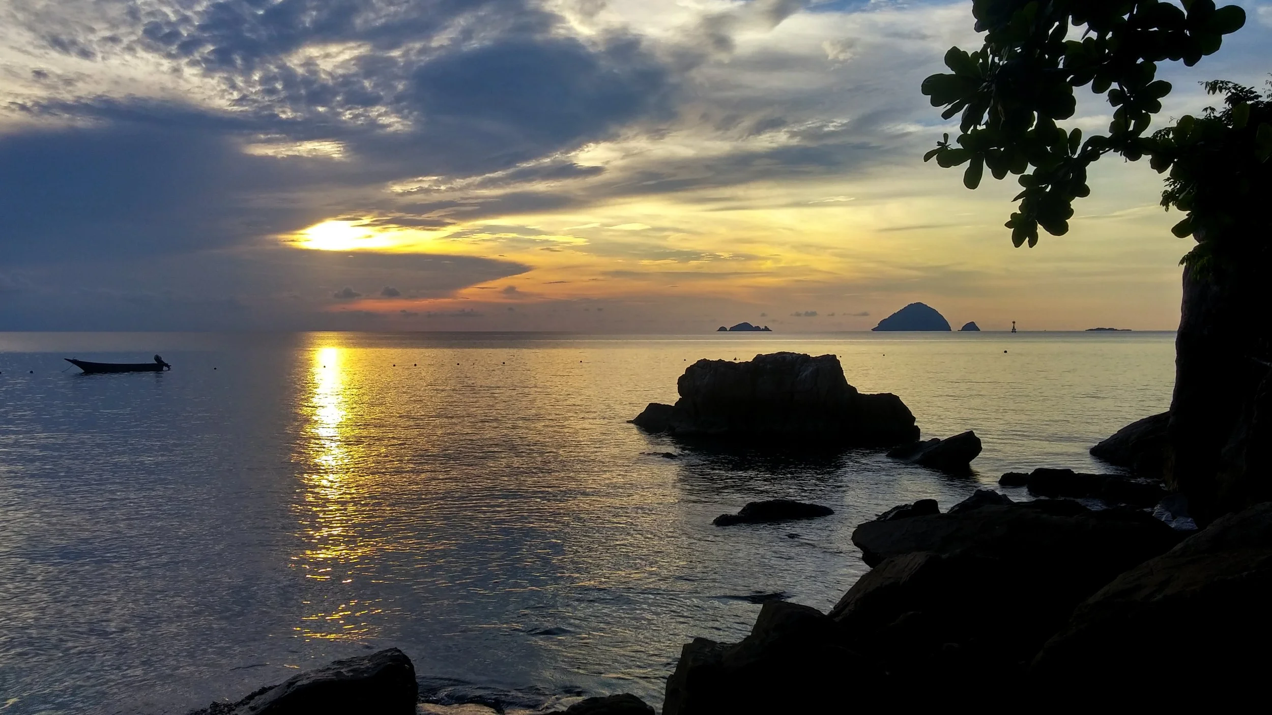 A sunset had lit up the sky with golden and pink hues. in the water, the silhouette of a fishing boat and outcroppings of rocks dominate the image