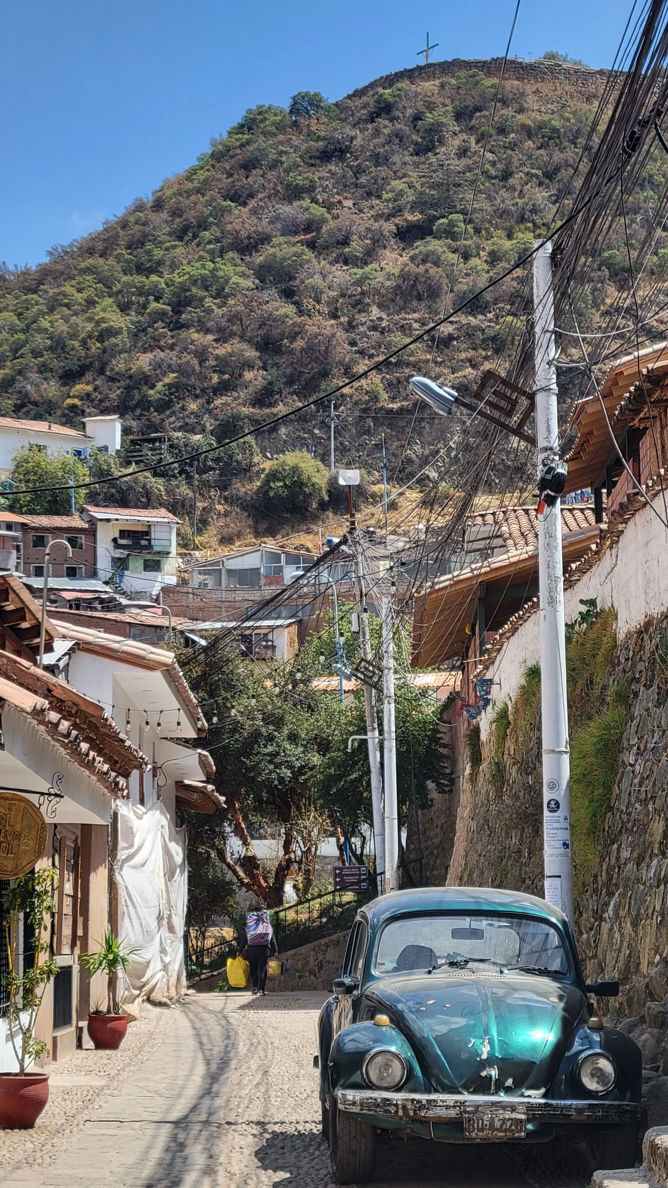 a green-blue VW beetle parked on the side of the street, a hill rises in the distance