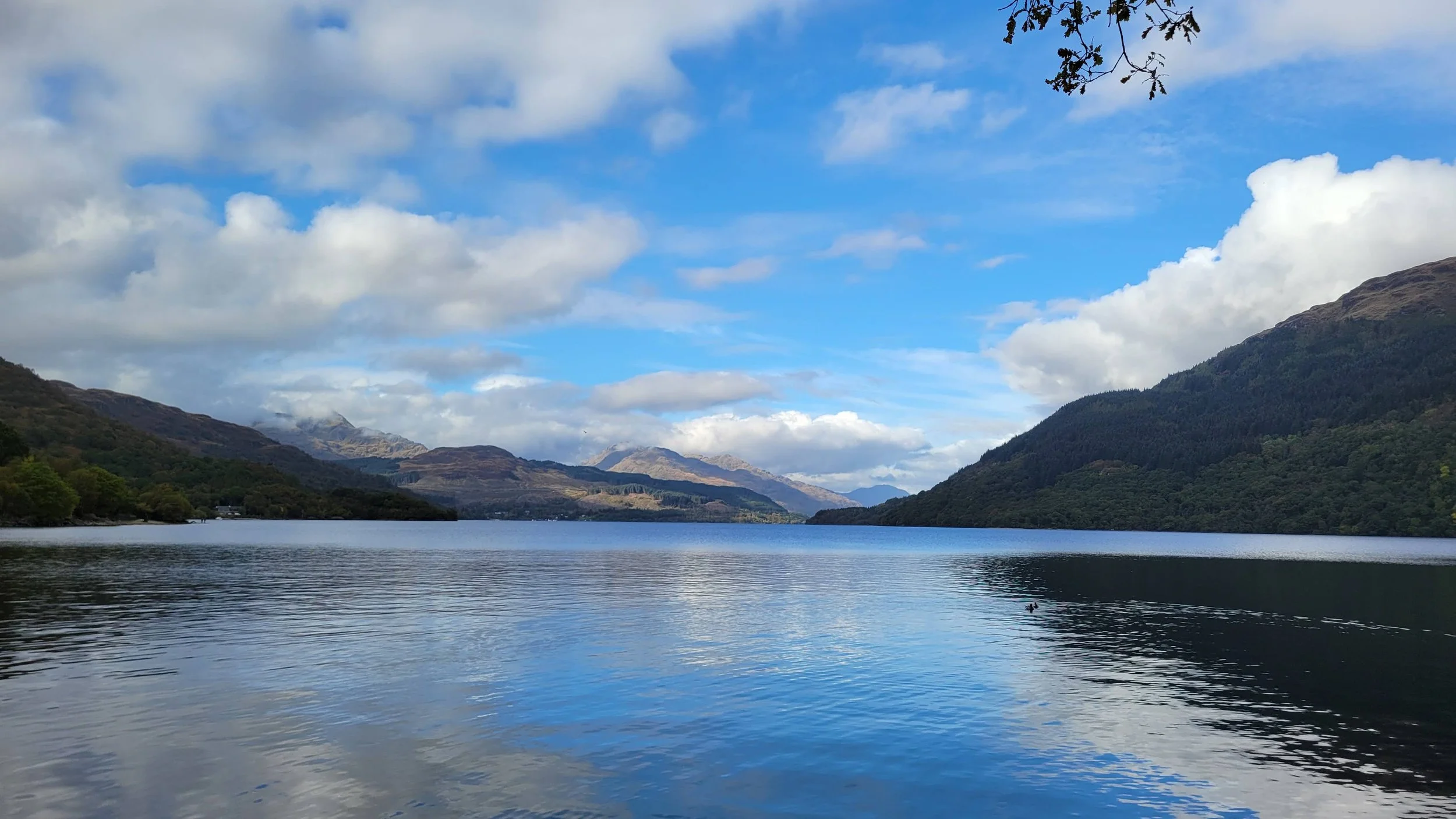 calm water of loch lomond white clouds blue skies small munros in background