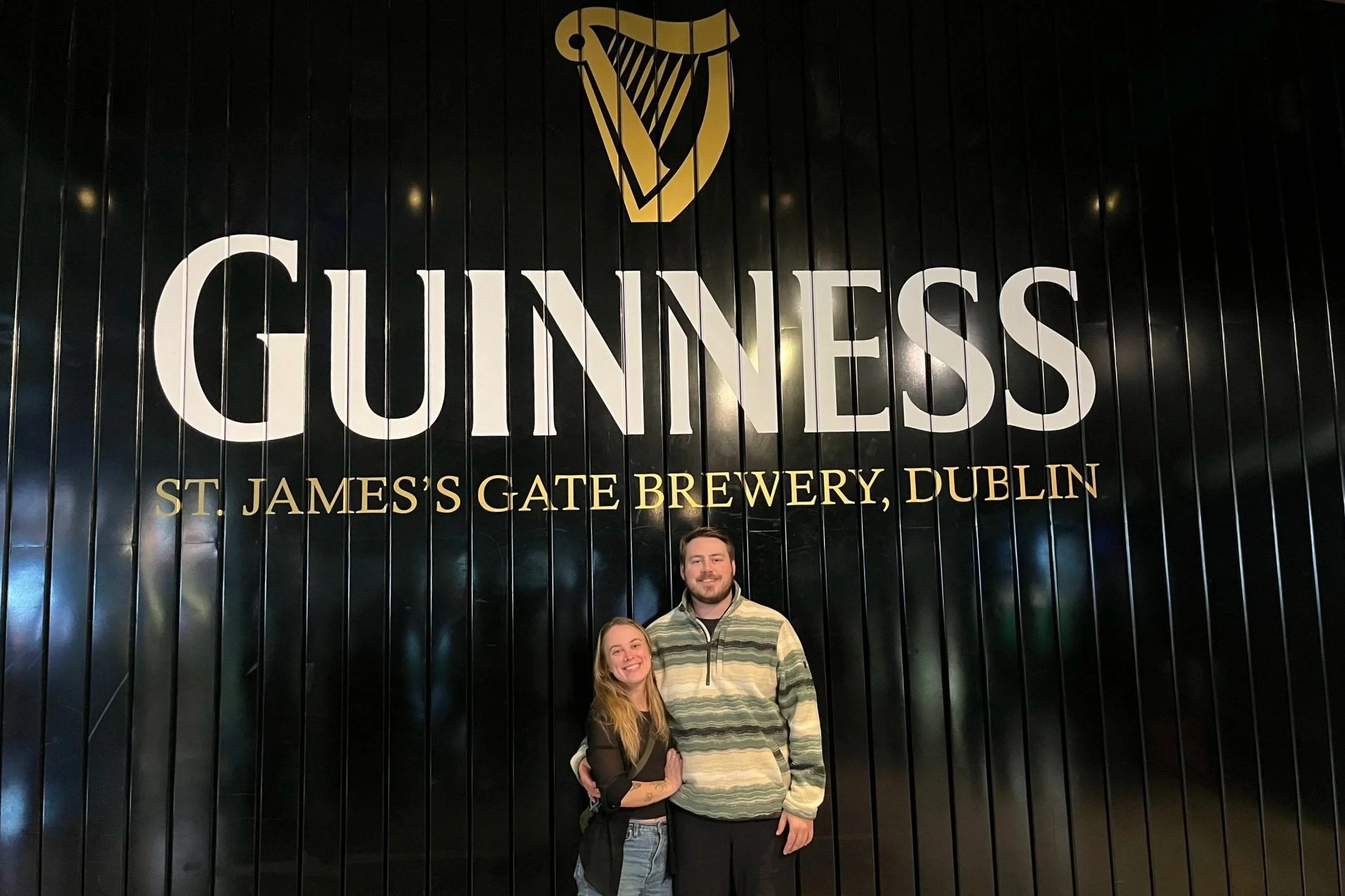 Tyson and Megan standing in front of black wood panelled wall that says "Guinness St James's Gate Brewery, Dublin"