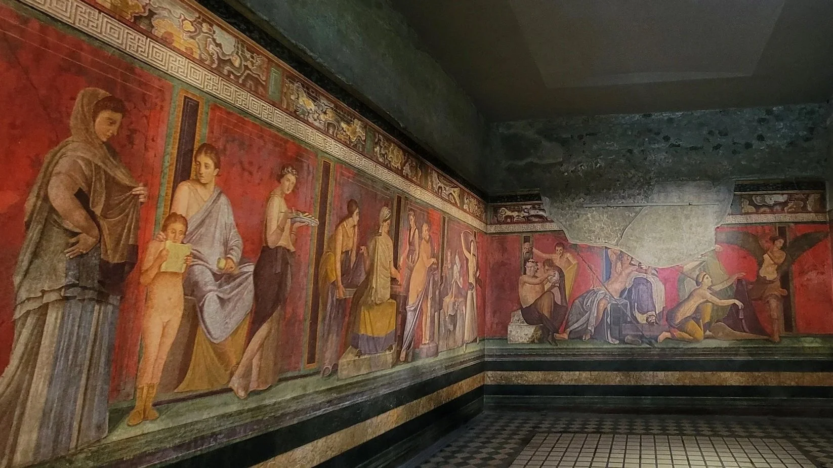 bright red walls with detailed fresco paintings of life size people in the villa of mysteries in pompeii