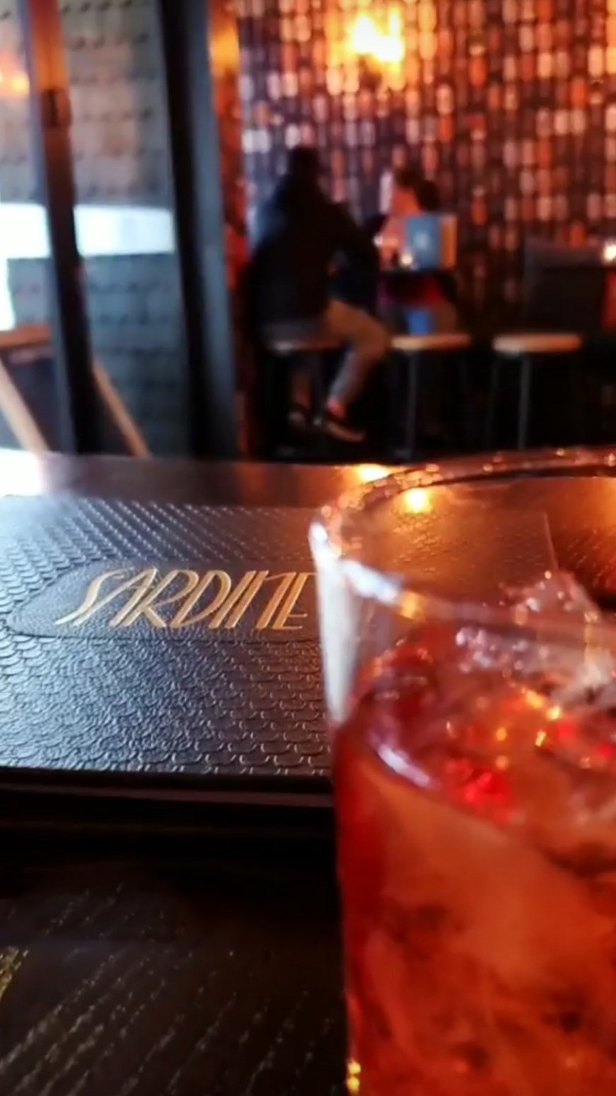 A negroni in a low lit room with the Sardine menu in the background.