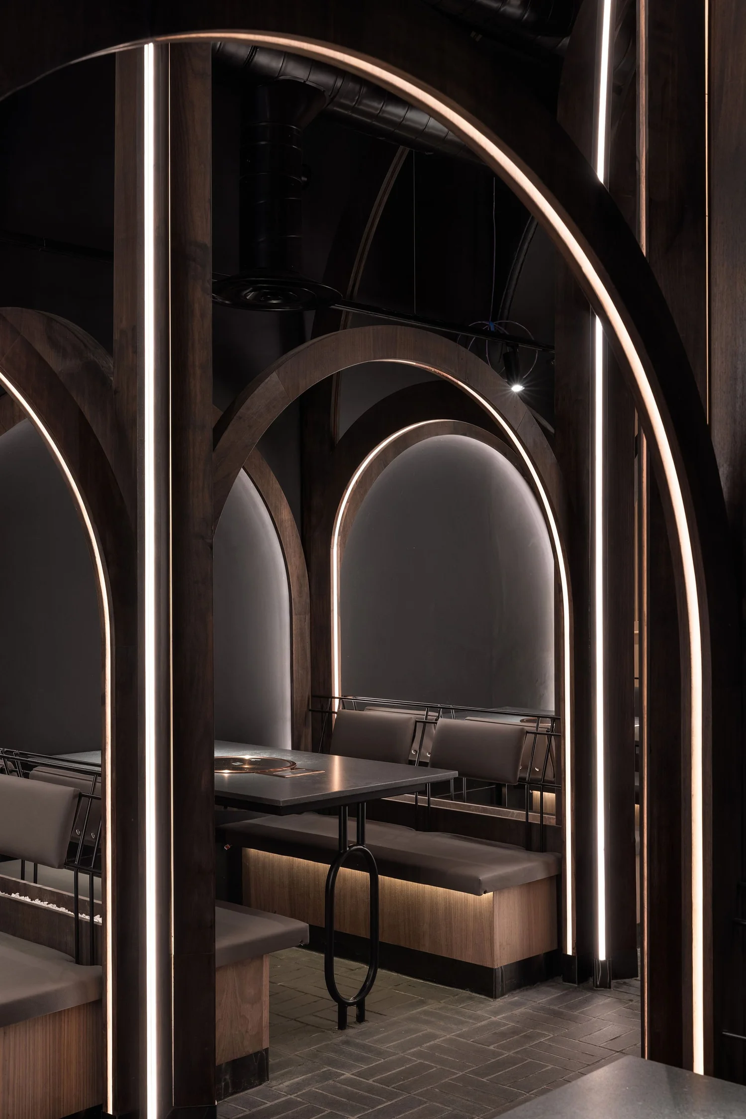 Illuminated timber arches framing upholstered dining booths and inset barbecue tables at Soom.