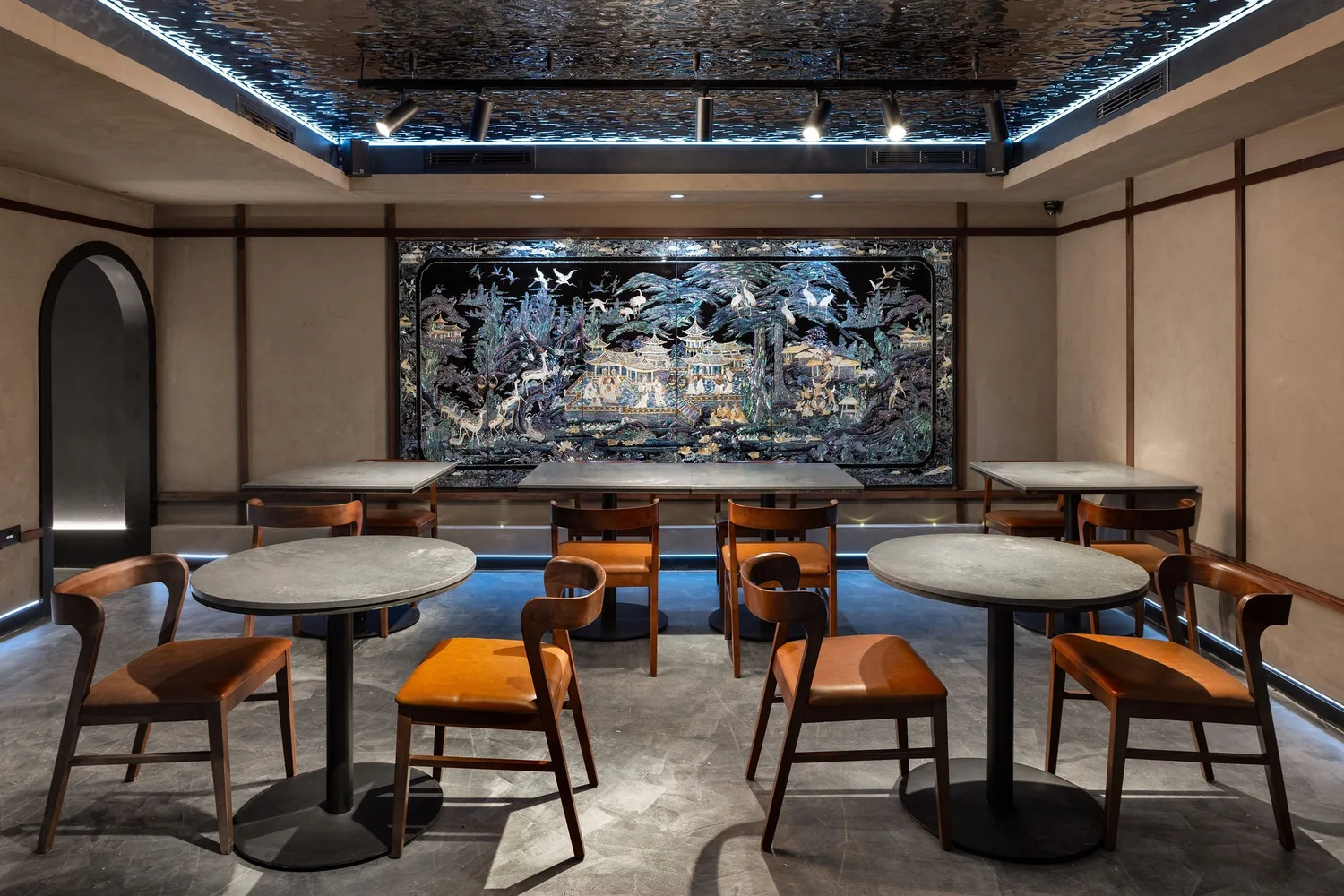 Soom basement dining room with timber chairs, a mother-of-pearl artwork and a rippled reflective ceiling.
