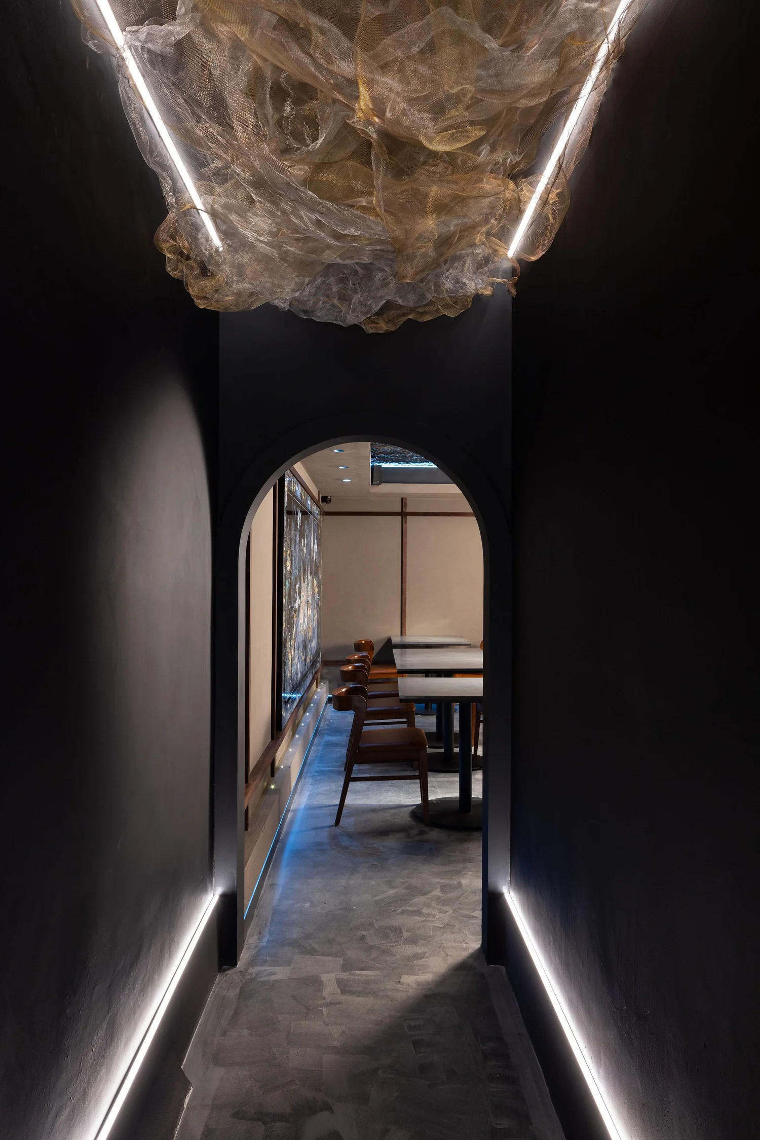 Dark arched passage at Soom with a sculptural mesh ceiling installation and floor-level lighting.