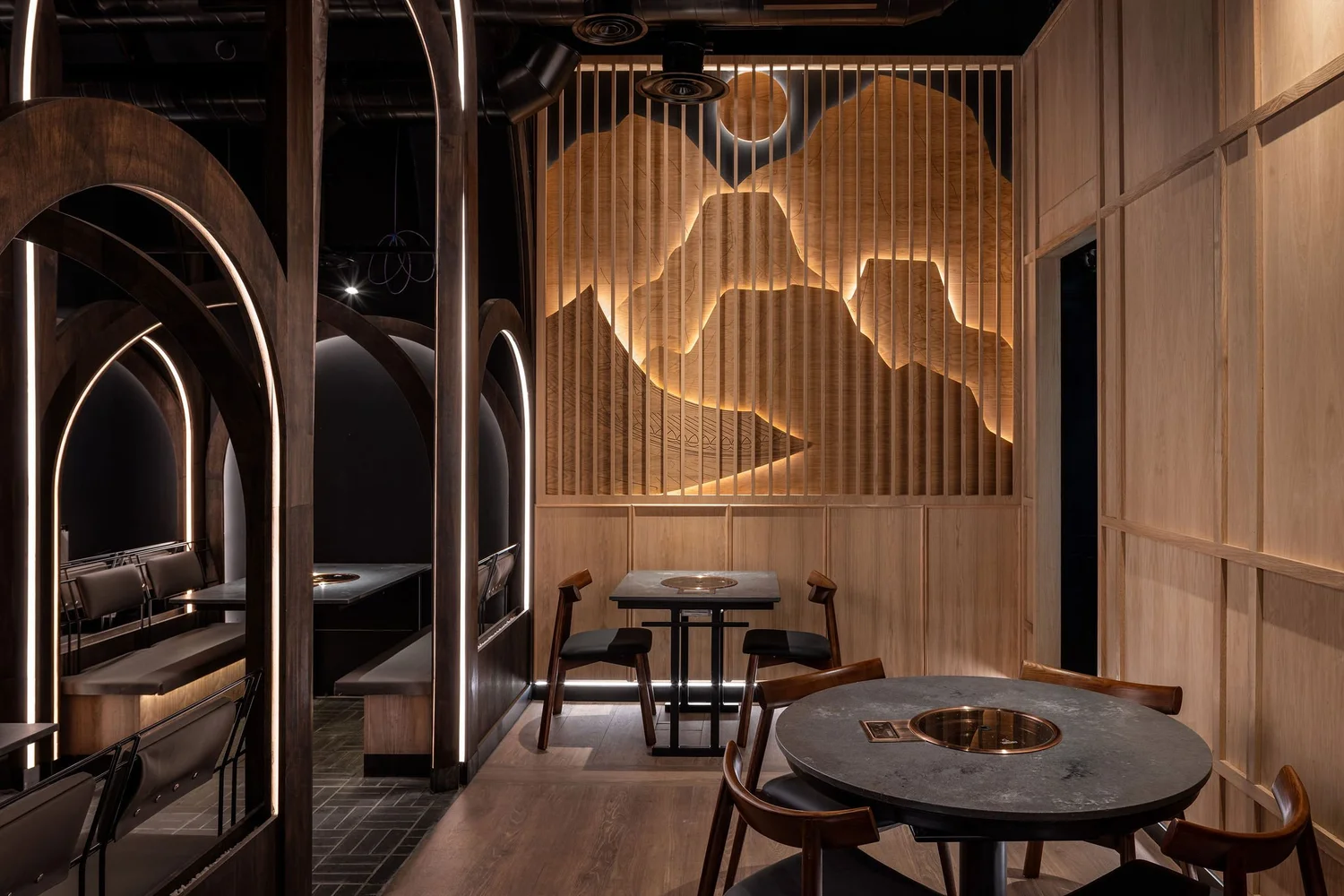 Timber dining area at Soom with illuminated mountain forms behind vertical slats and an adjacent arched booth.