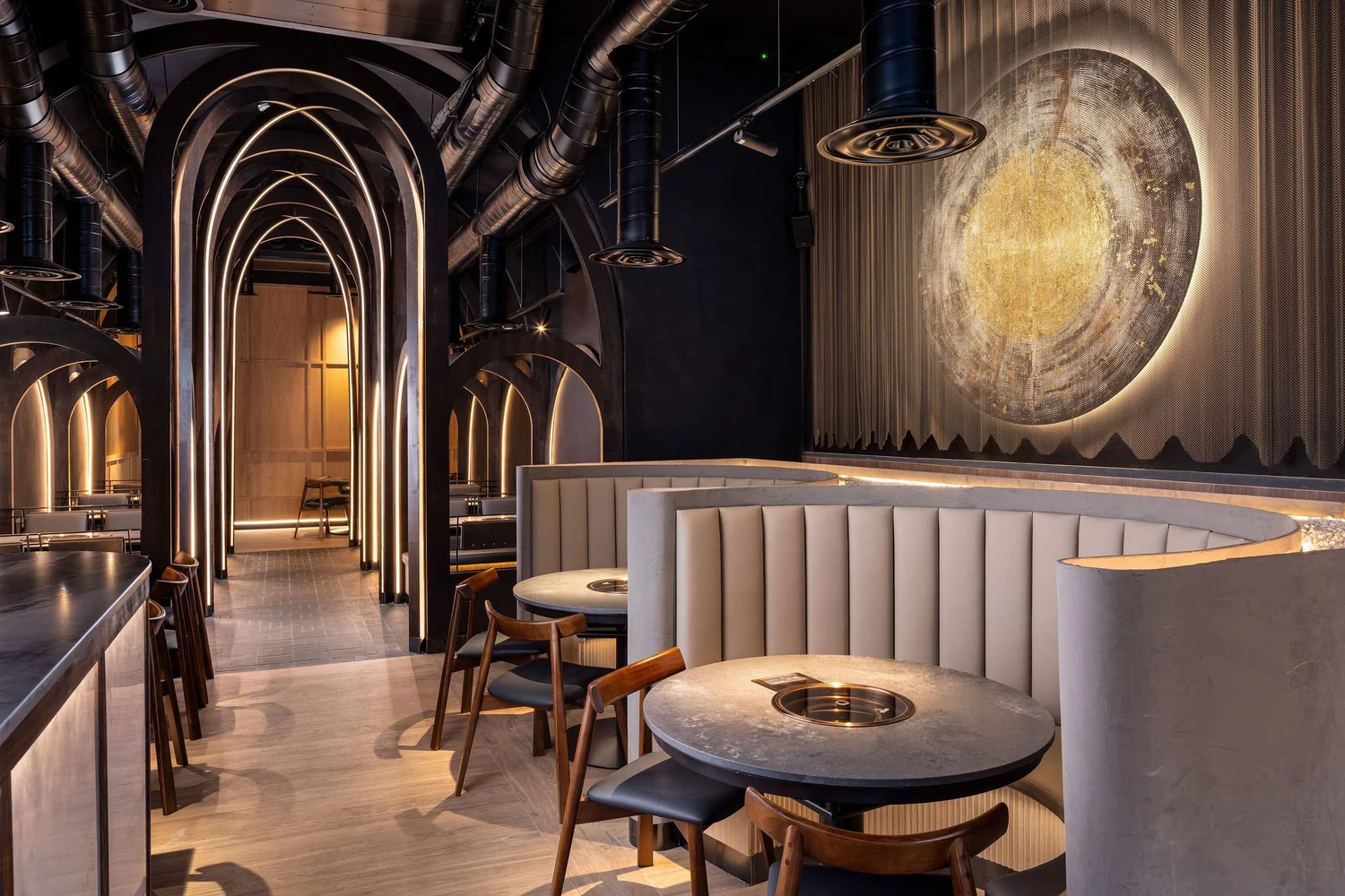 Curved banquette seating beside the illuminated arches and large circular gong at Soom, London.