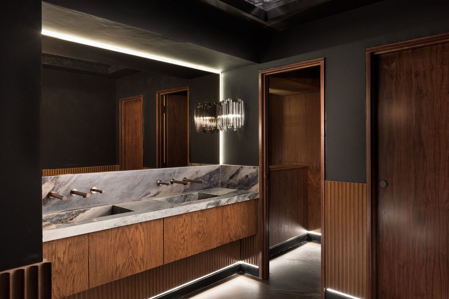 Soom washroom with a veined stone vanity, timber cabinetry and a large illuminated mirror.