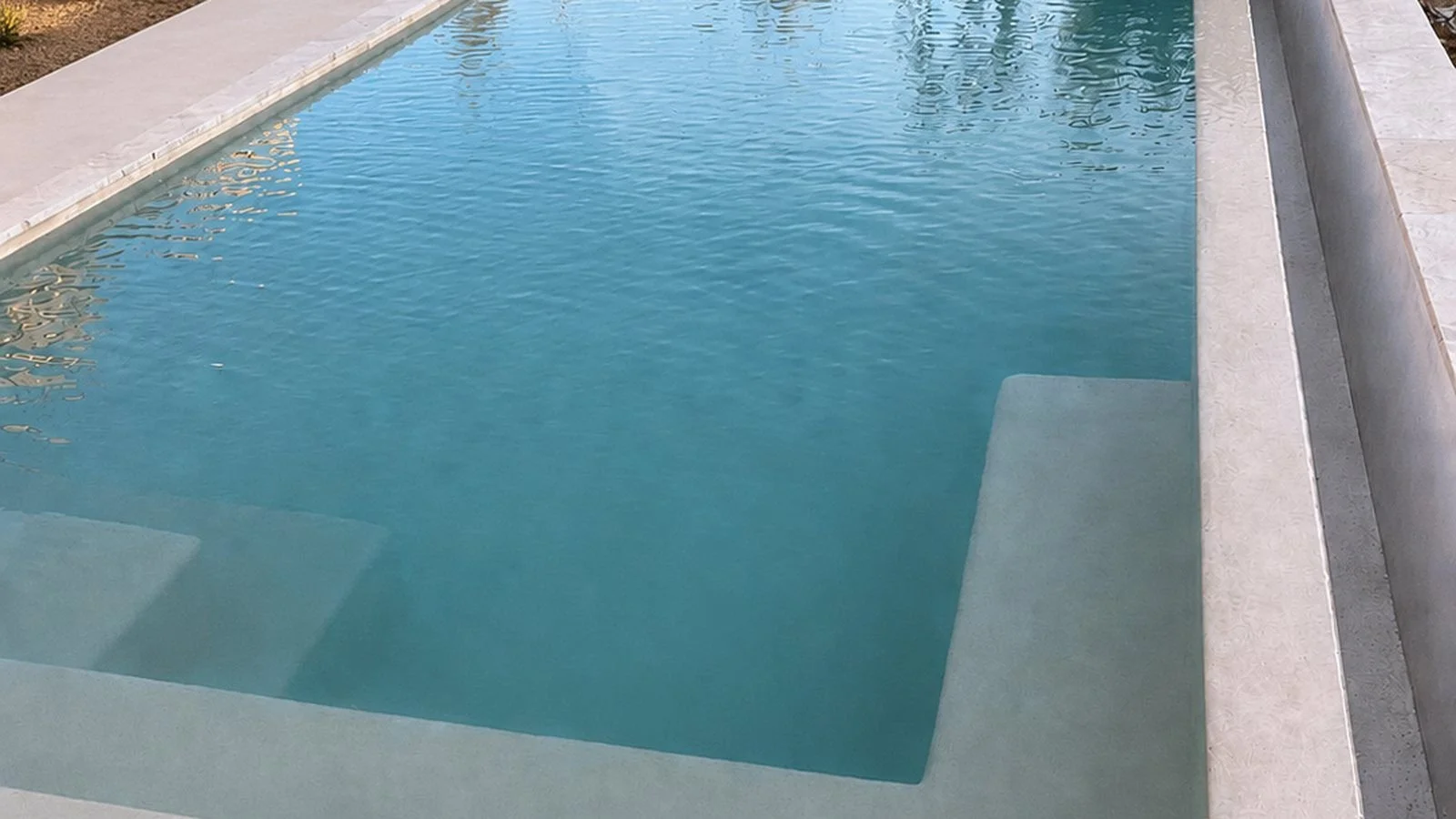 Piscine moderne en béton avec des escaliers immergés, de l'eau claire et calme, entourée d'une terrasse en pierre