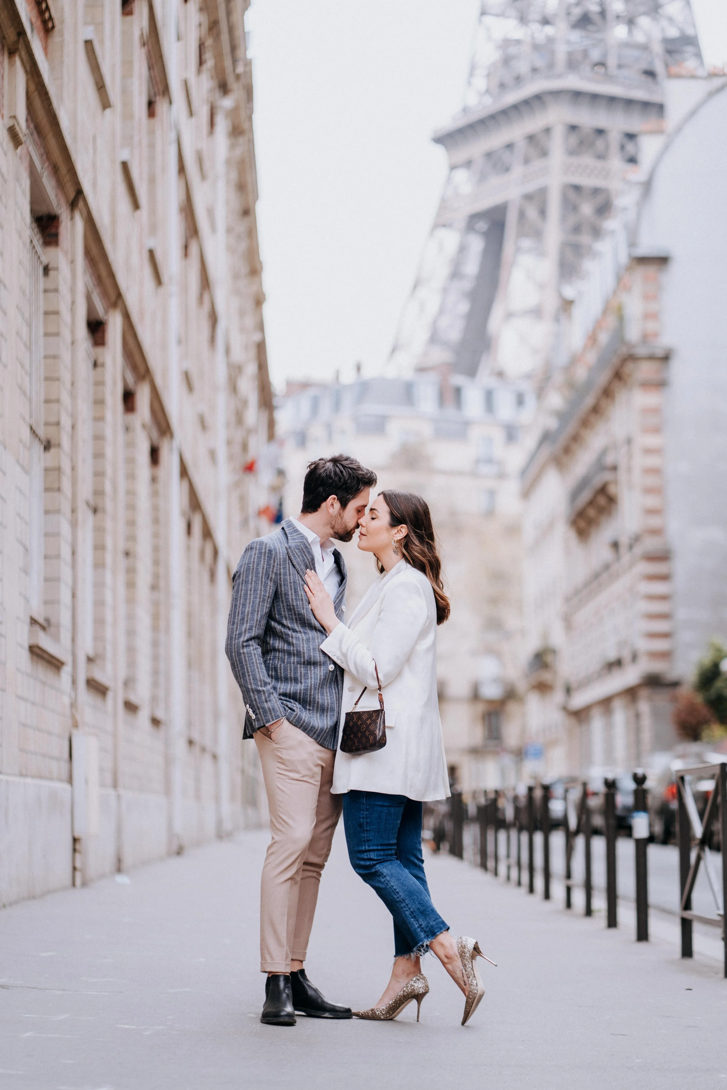 A couple standing close together on a Paris street with the Eiffel Tower in the background, engaged in an intimate moment.