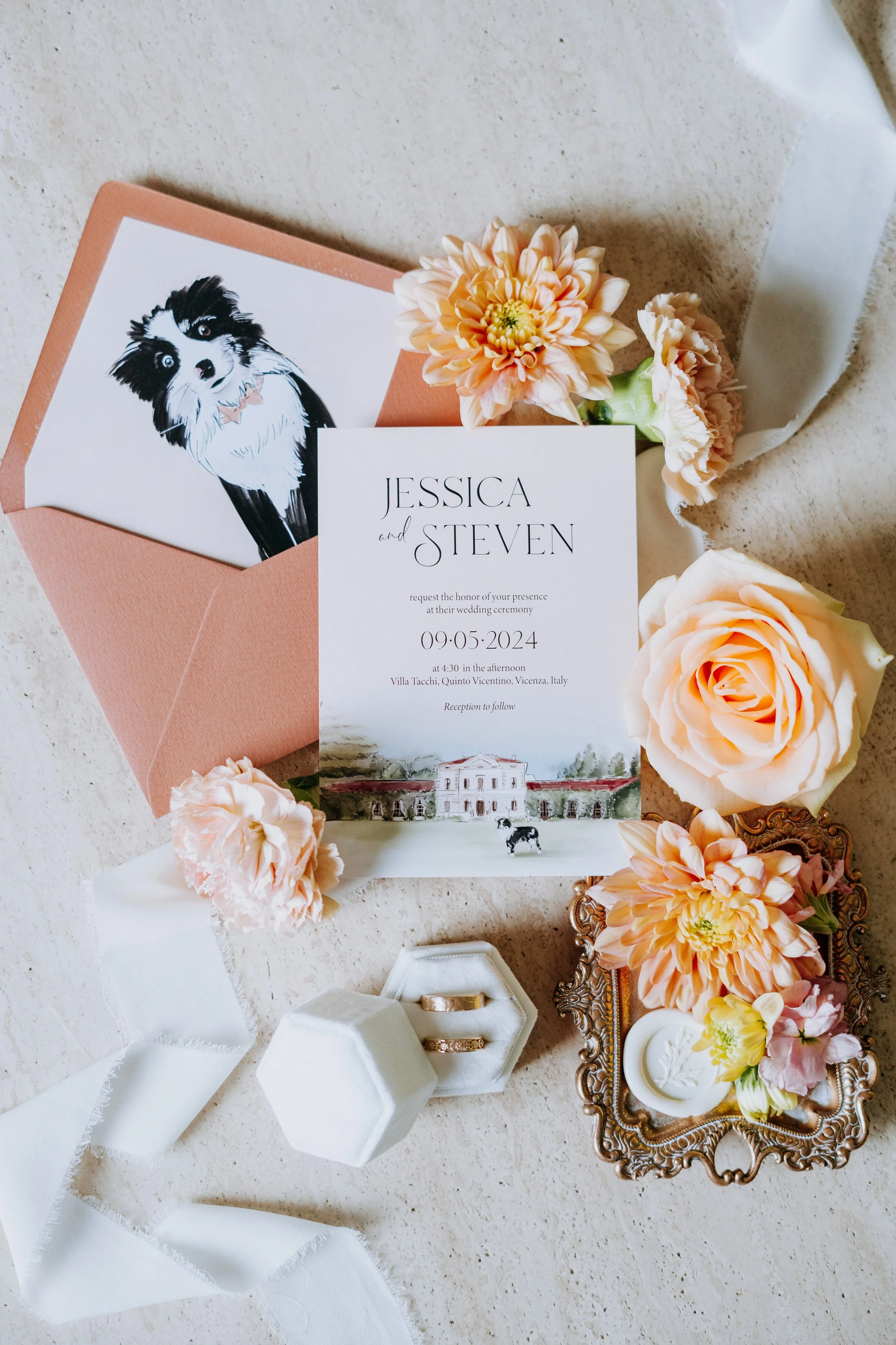 Wedding invitation with flowers, rings, and decorative items on a light-colored surface.