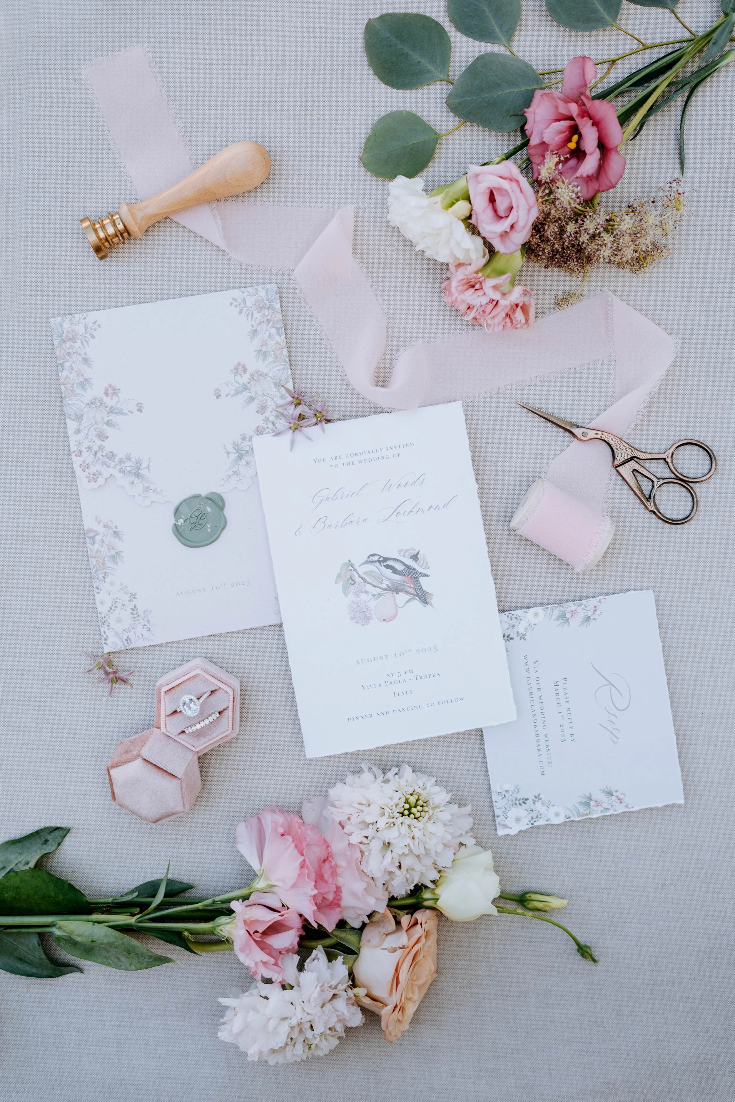 Wedding invitation suite with flowers, jewelry, and craft supplies on fabric.