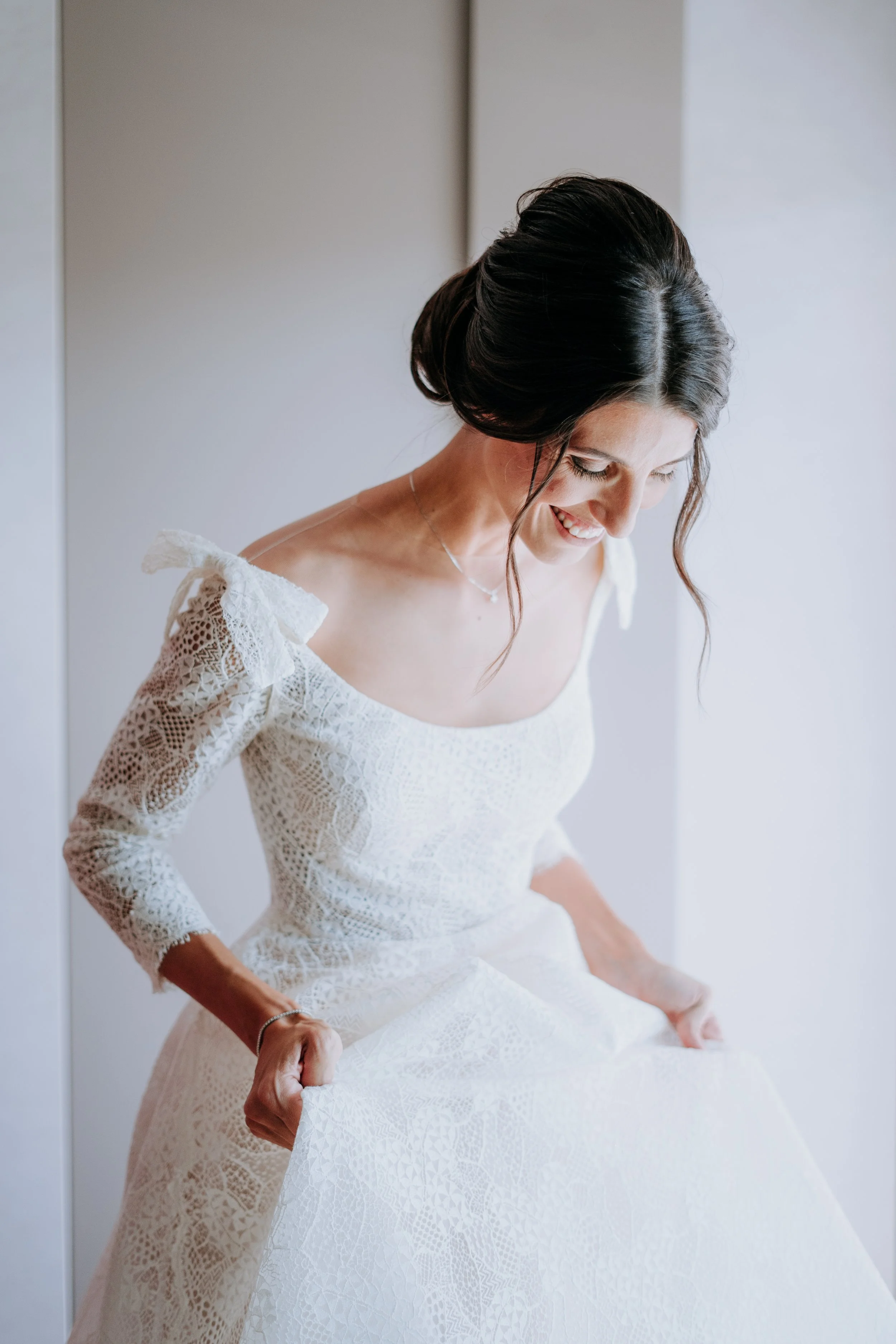A bride in a white lace wedding dress smiling while holding up her dress.