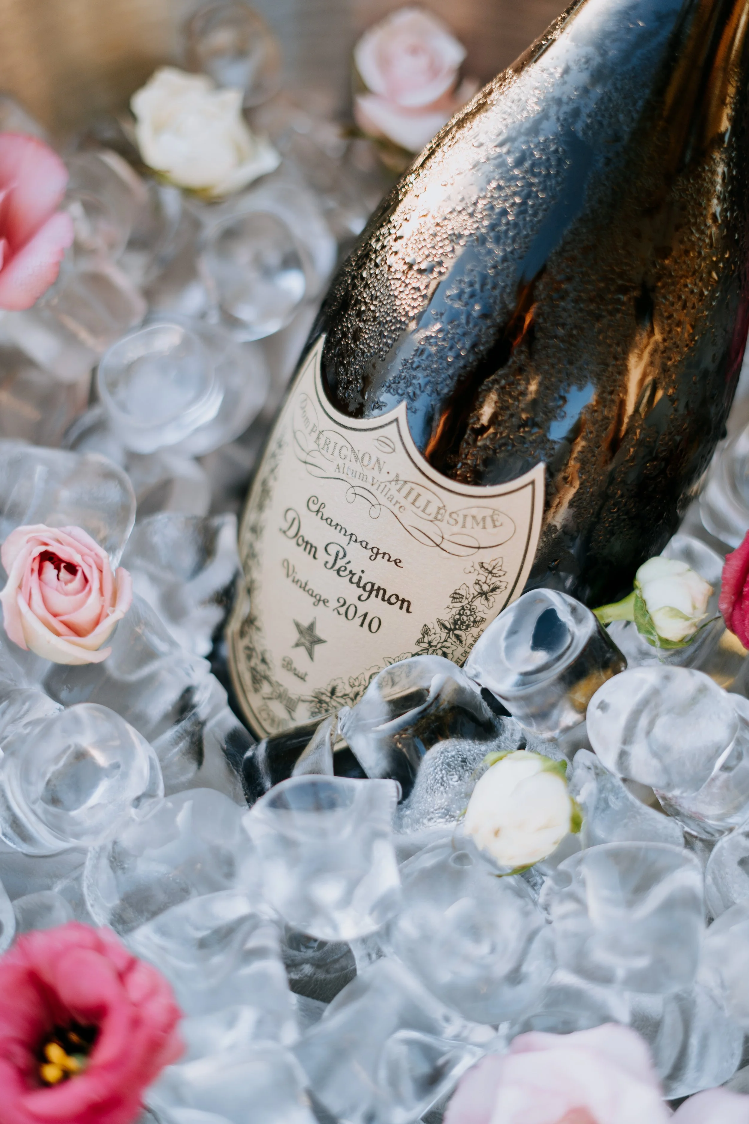 A bottle of Dom Pérignon champagne resting in a bed of ice and surrounded by pink and white flowers.