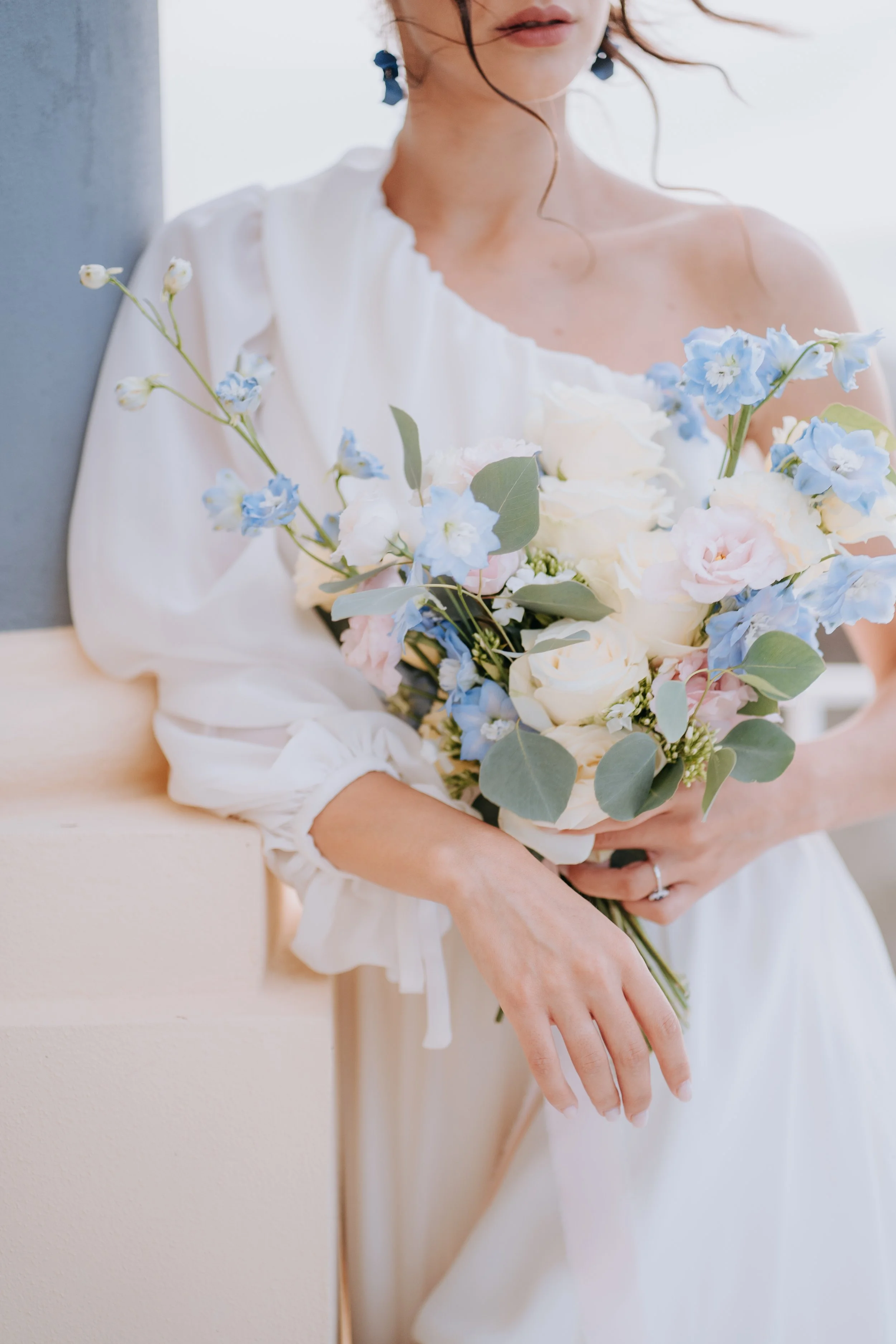 A woman in a white dress holding a bouquet of white and blue flowers with eucalyptus leaves.