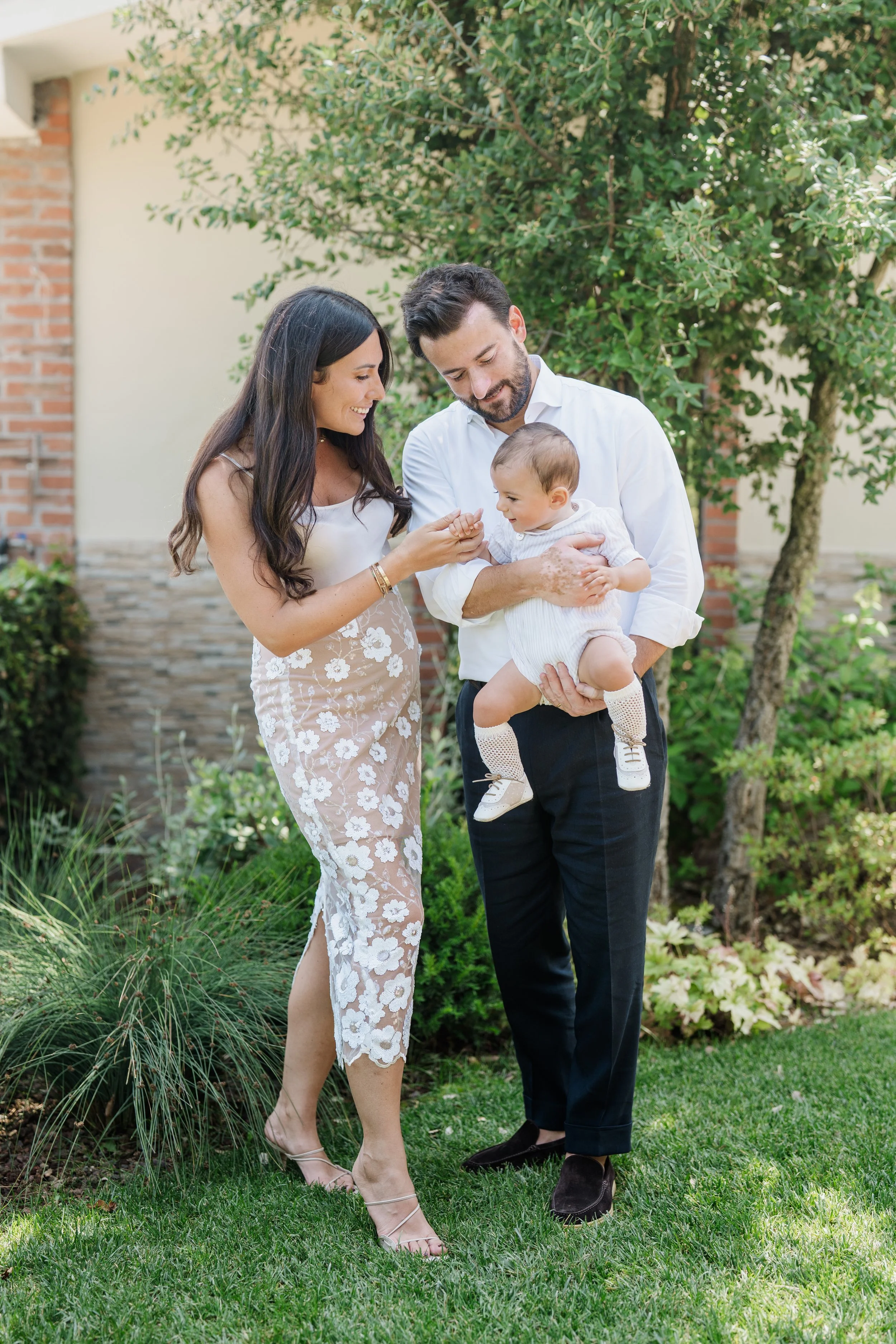 A family of three, a woman, a man, and a baby, enjoying time together outdoors in a garden.