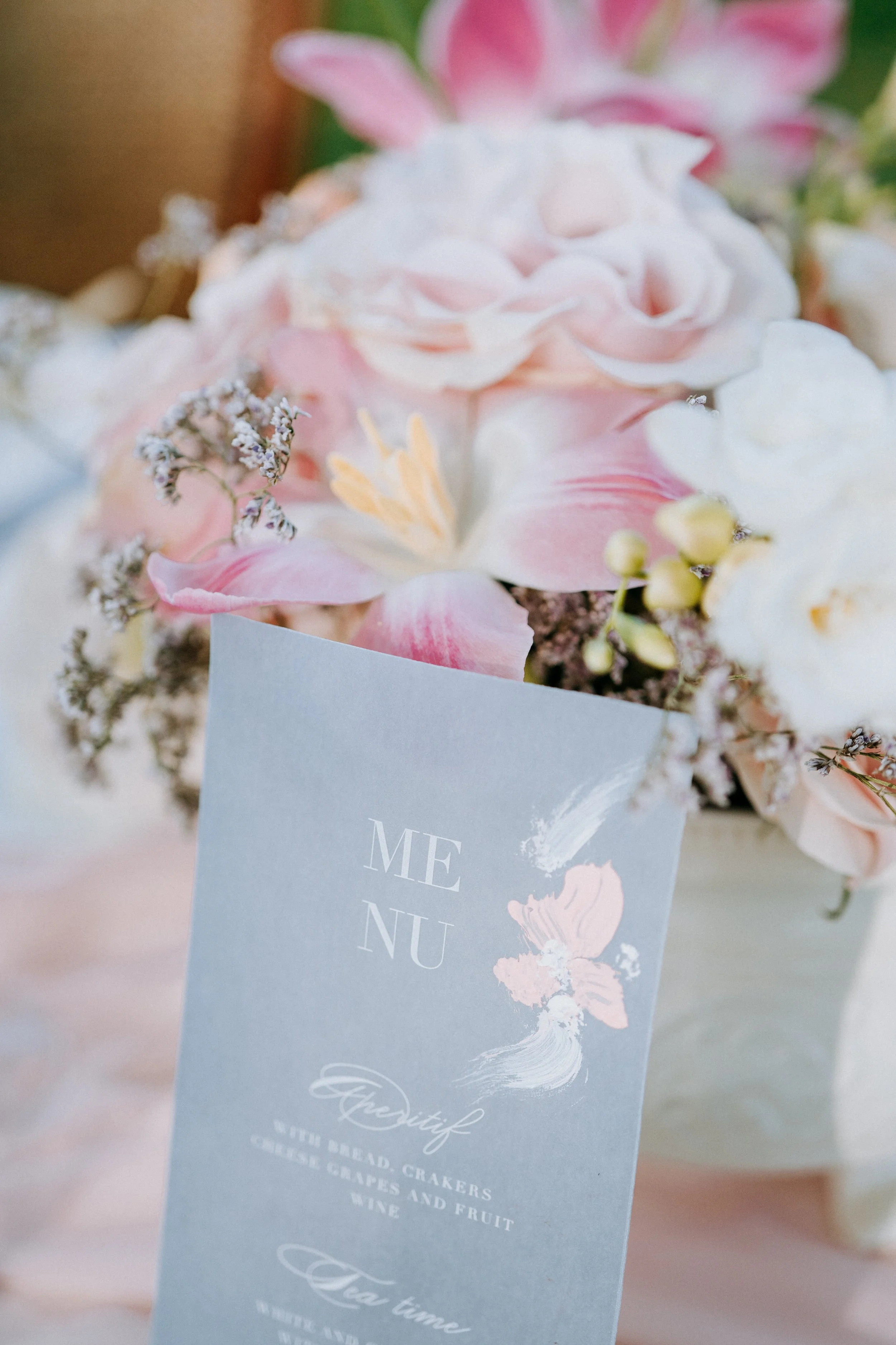 A bouquet of pink and white flowers with a light blue menu card placed among the flowers