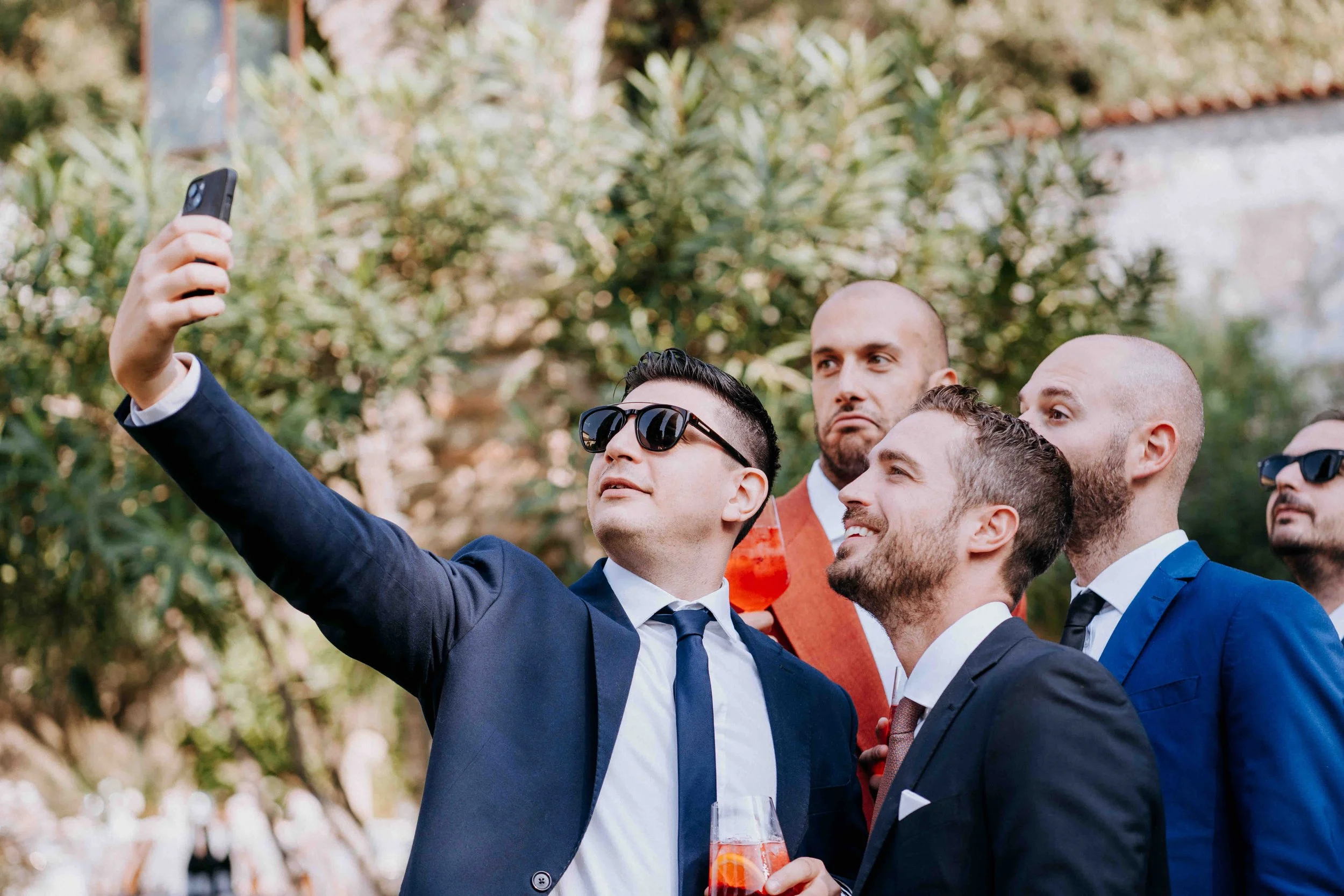 Group of men in suits taking a selfie outdoors during a social event.