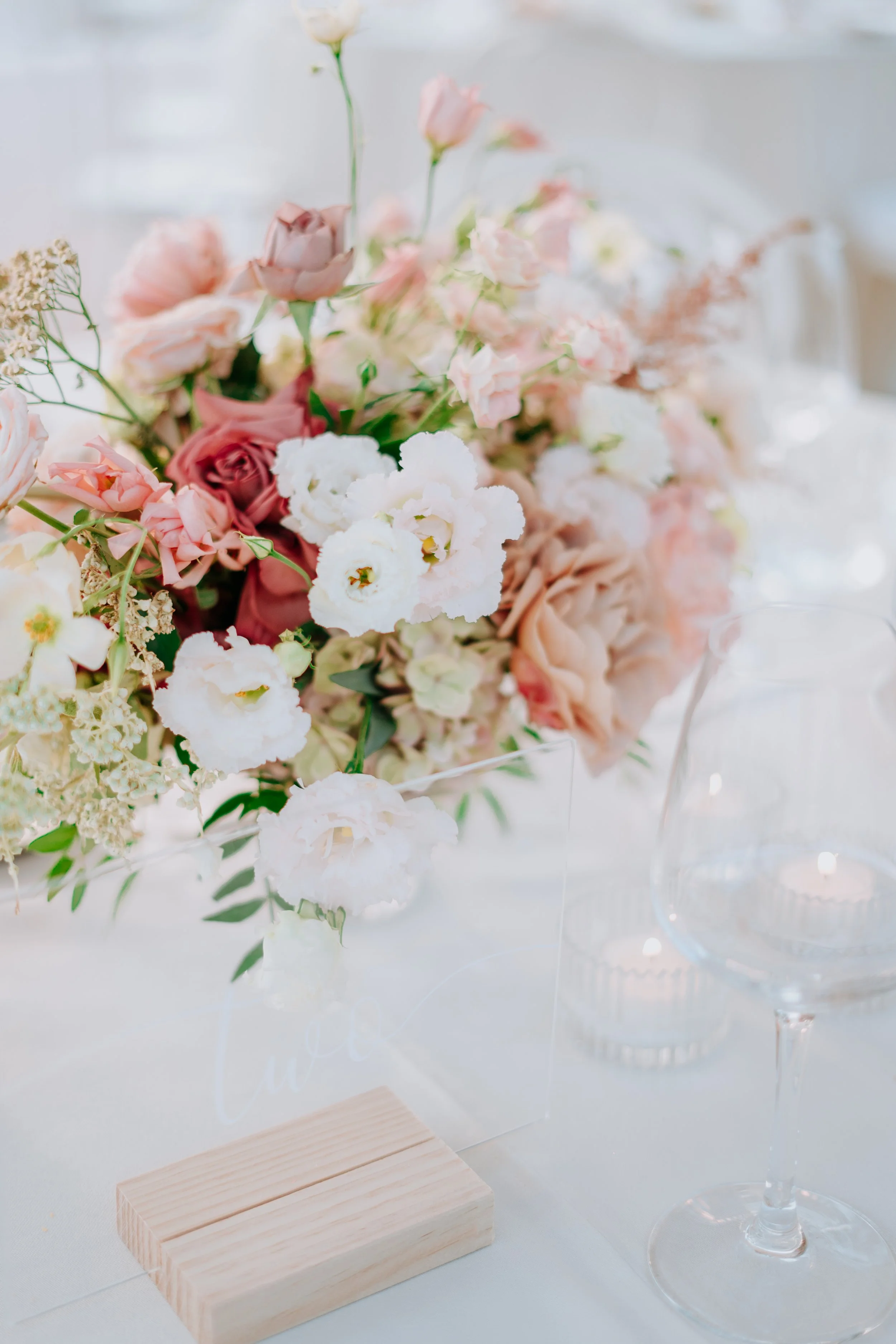 A romantic floral centerpiece with pink, white, and blush roses and other flowers on a table set for a special occasion.