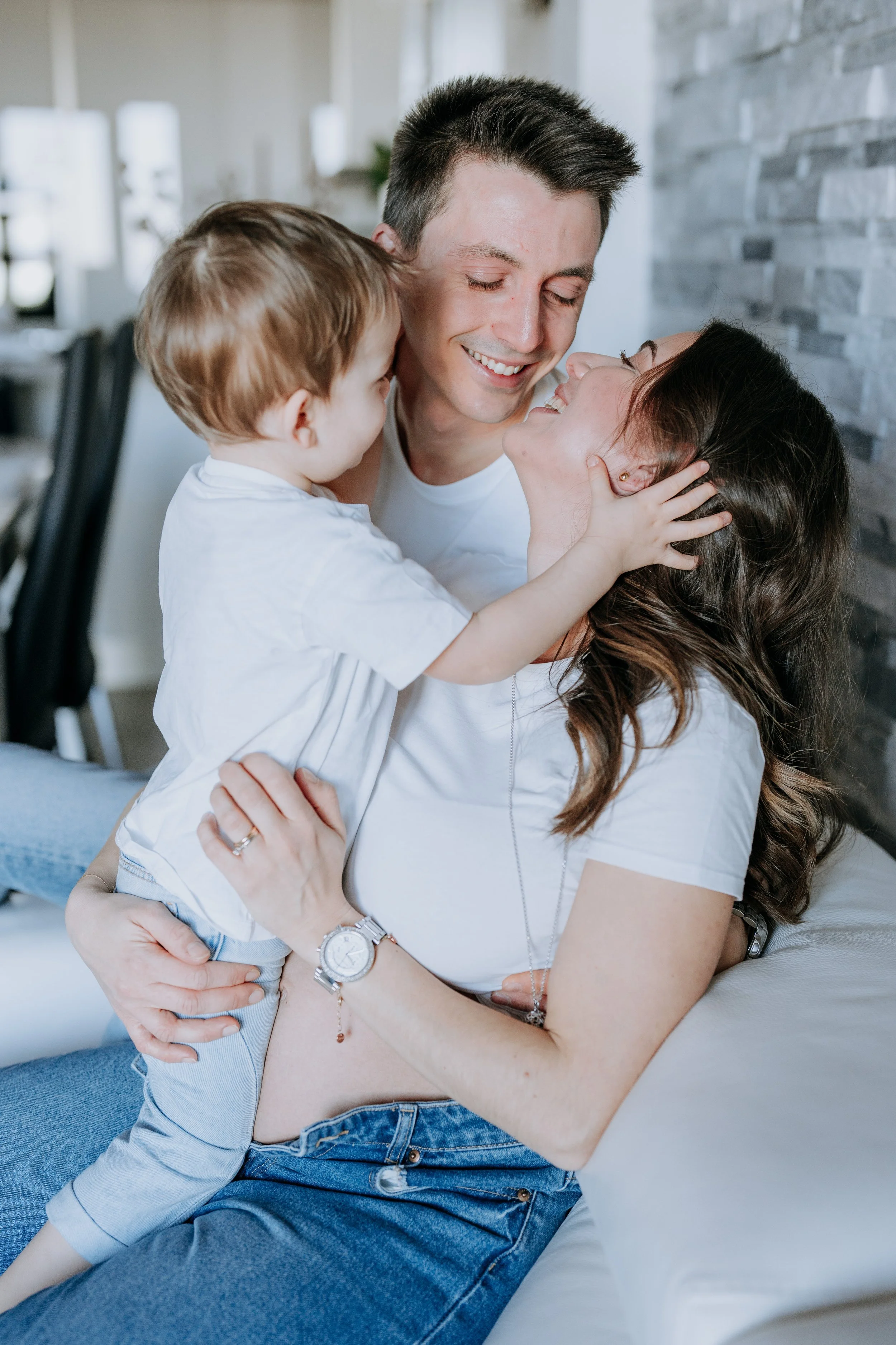 A happy family moment with a woman, a man, and a young child cuddling and smiling together indoors.