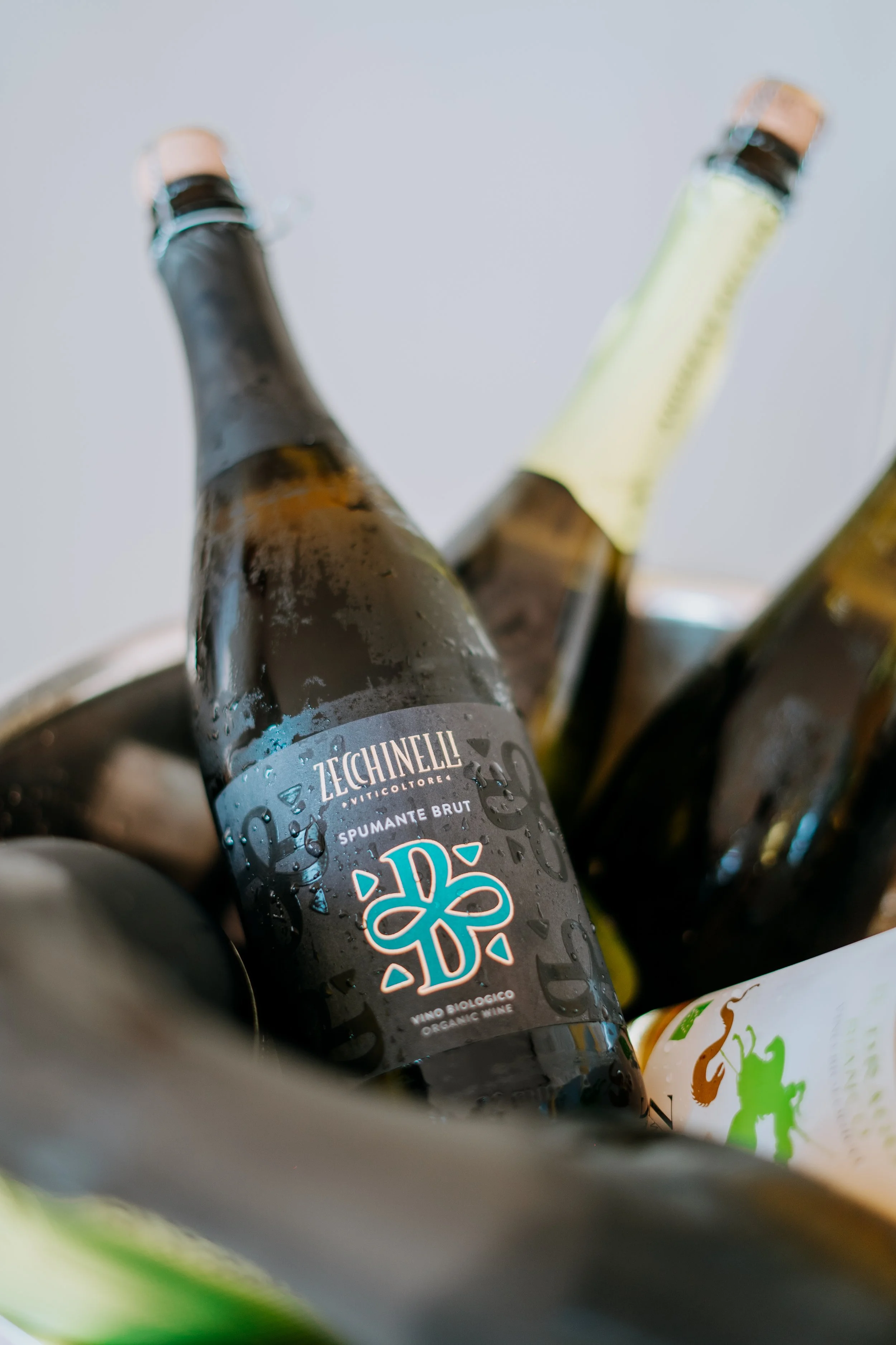 Close-up of a bottle of Zechinelli Spumante Brut organic sparkling wine among other bottles, with condensation on the bottle, in a cooler or ice bucket.