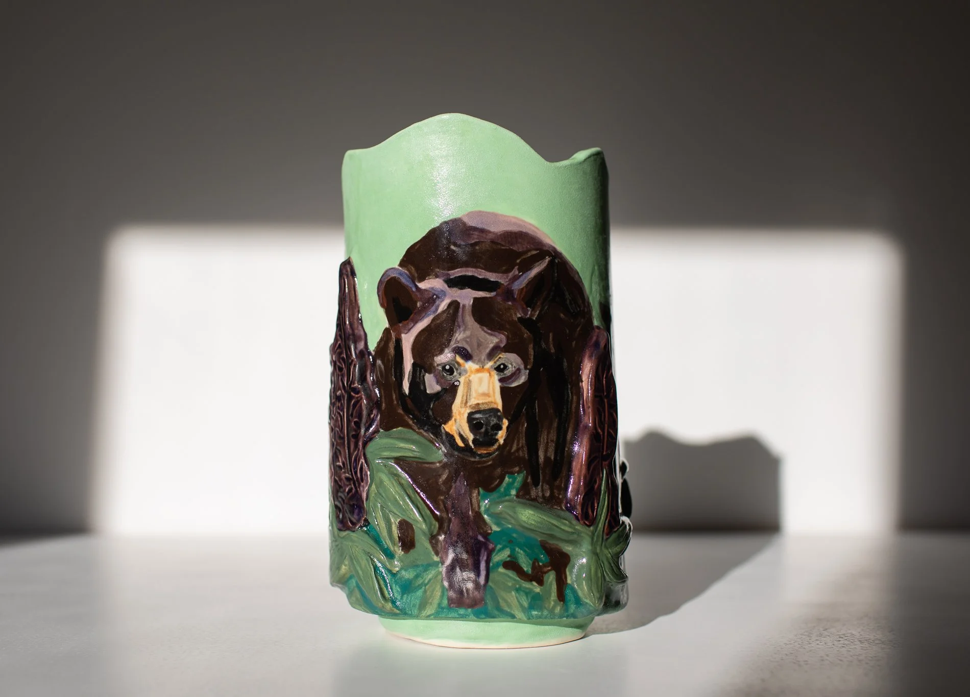 Colorful ceramic vase with a painted image of a bear in a lupine field, set on a white surface.