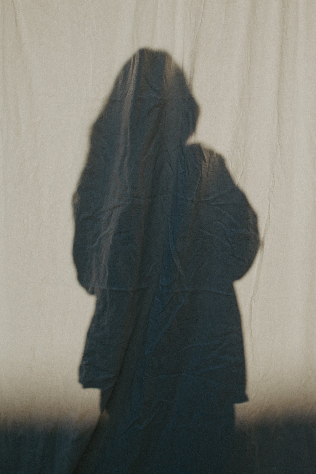 A shadow of a woman with long hair cast on a fabric curtain.