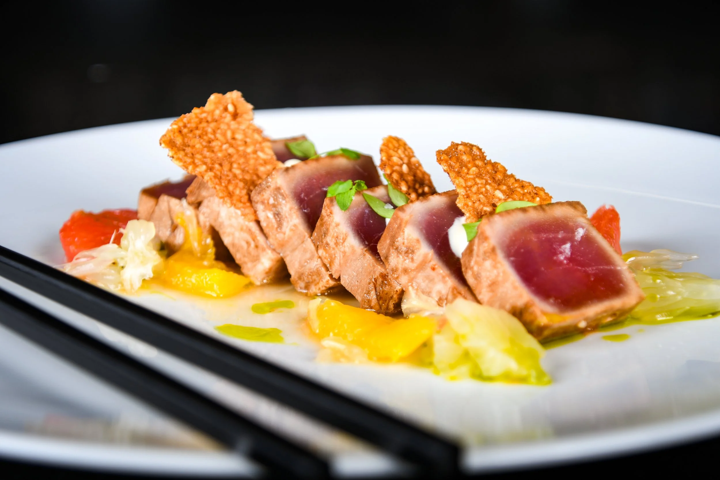 Servierte Vorspeise mit rotem Thunfisch in Seetangkruste, auf Gemüse mit Soße und knusprigem Topping, auf weißem Teller